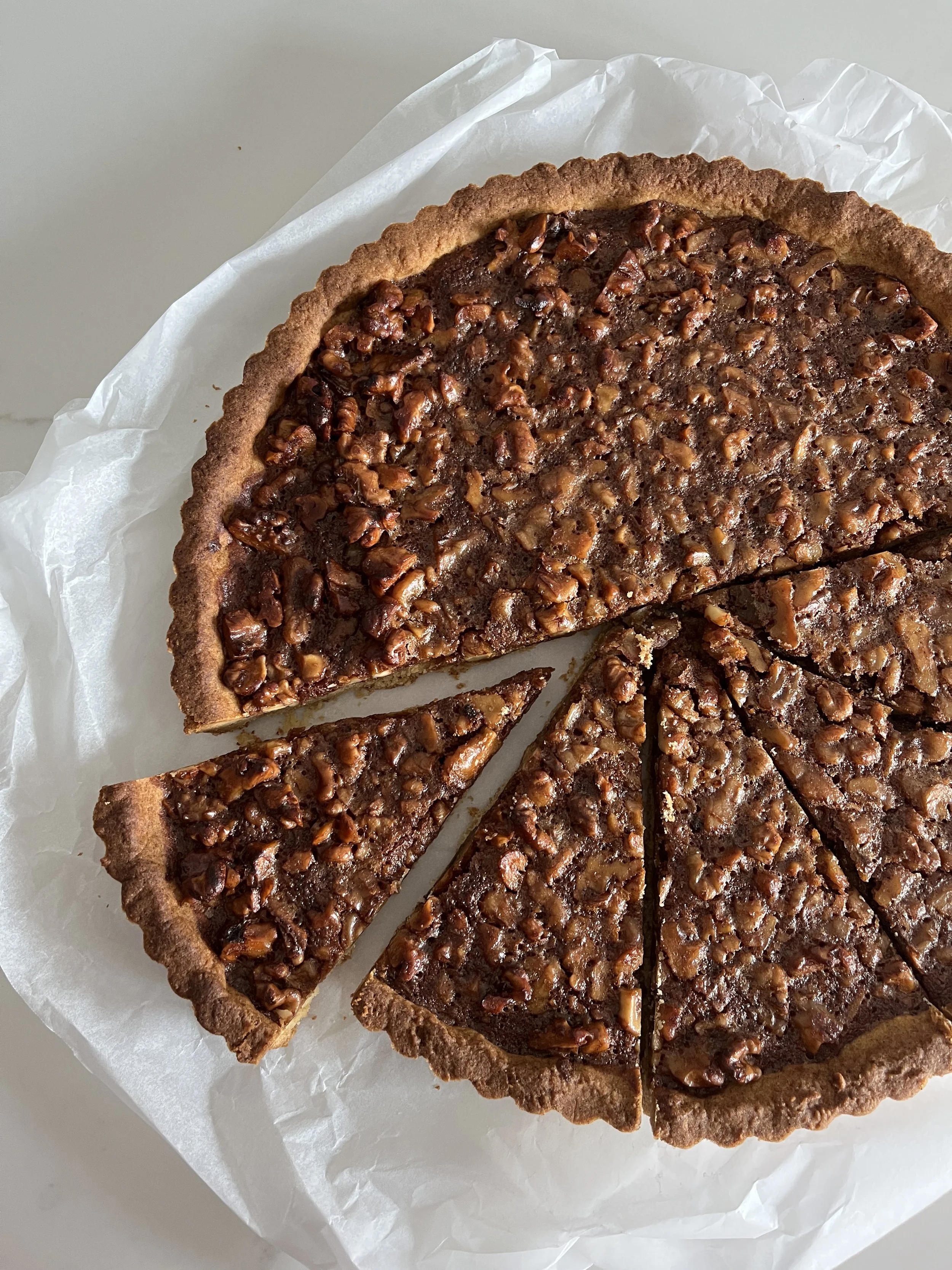 Chocolate pecan tart with sliced pieces on white parchment paper.