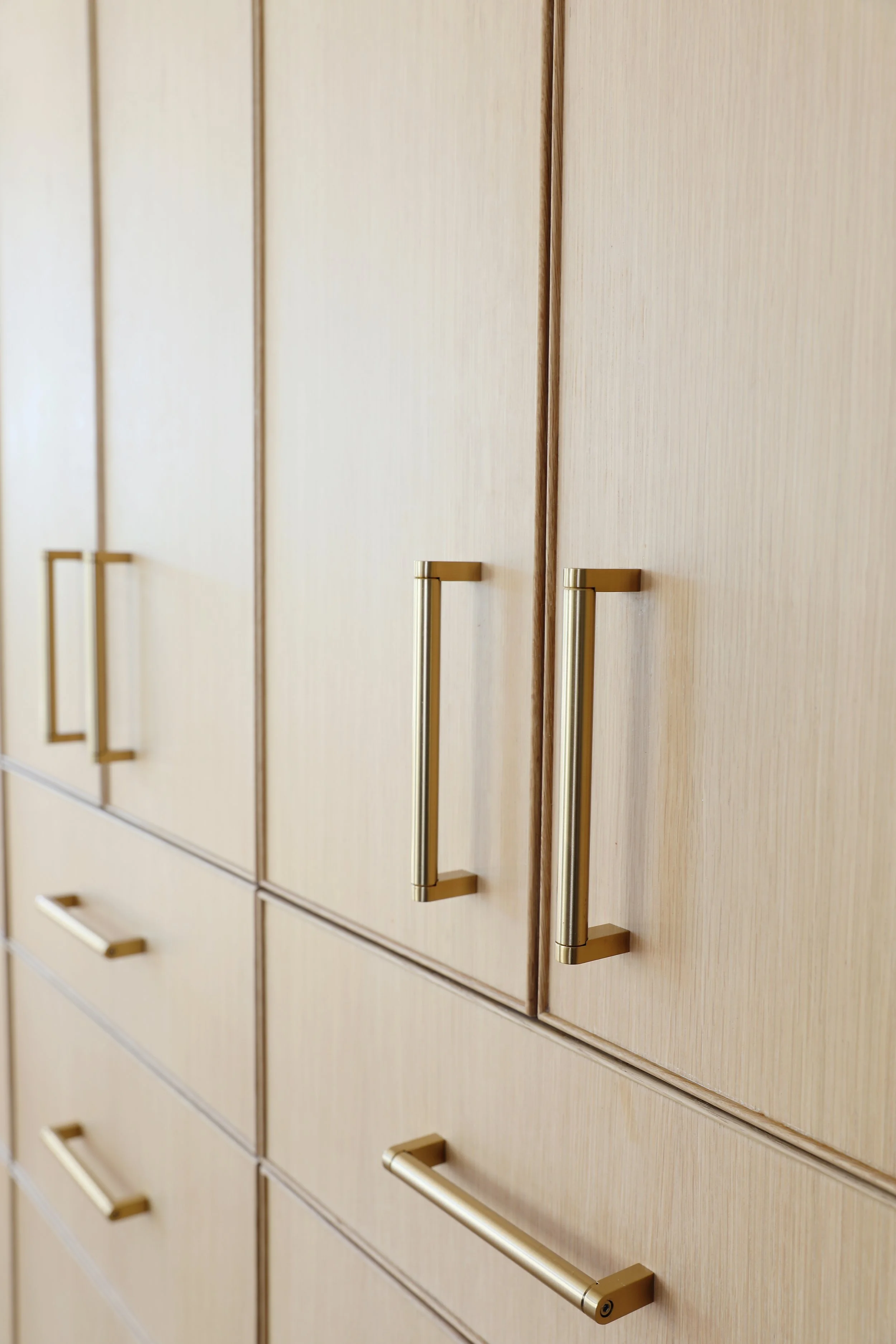 Close-up of beige wooden cabinets with gold-colored vertical and horizontal handles.