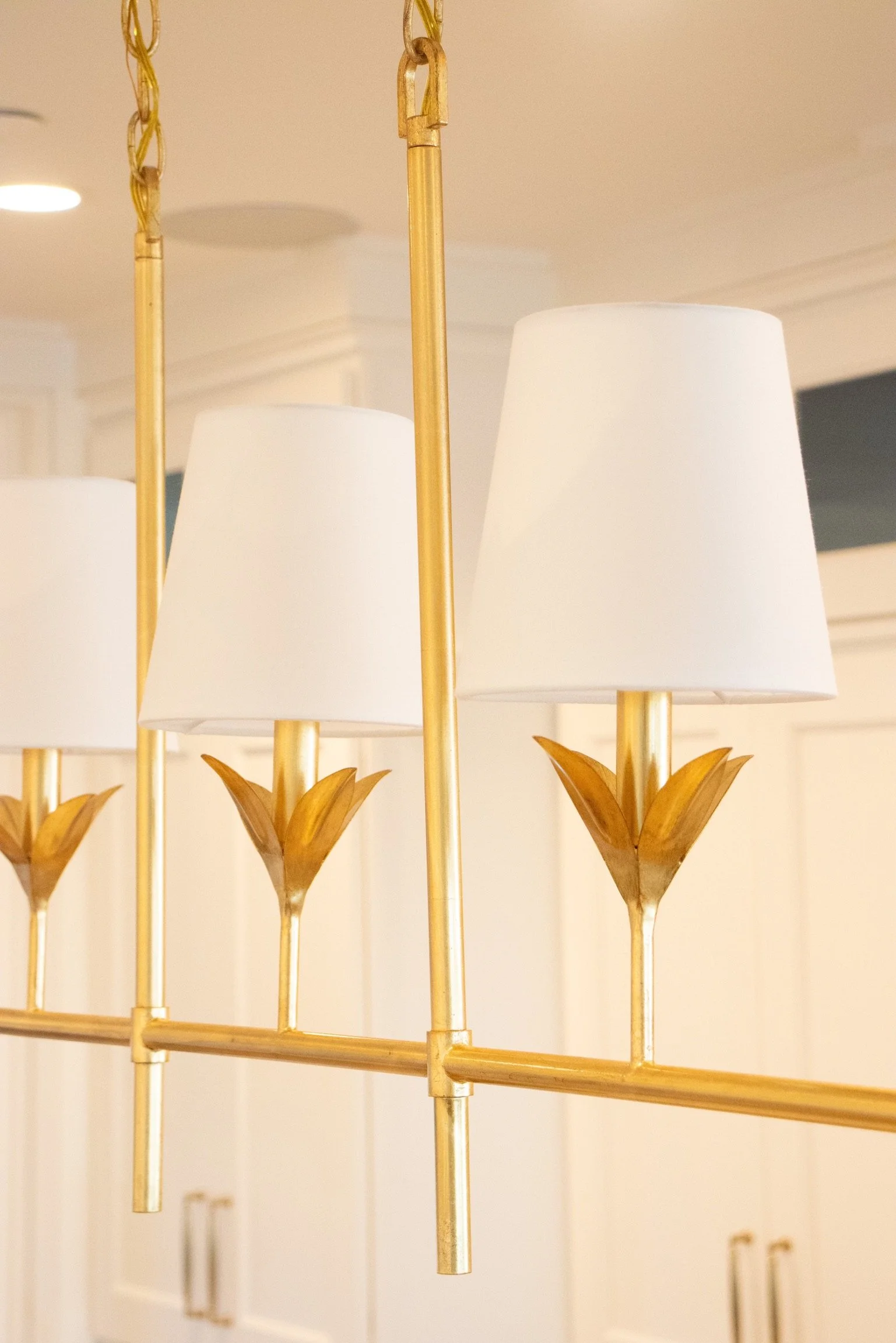 Close-up of a chandelier with white lampshades and gold-colored metal accents in a home interior.