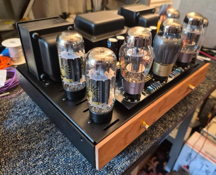 Close-up of a vintage electronic tube amplifier with glass vacuum tubes mounted on a wooden and metal chassis.