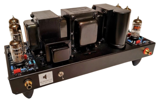 A black electronic device with large cylindrical components and glass vacuum tubes, likely a tube amplifier or audio amplifier, with gold-plated connection terminals and a label on the front.