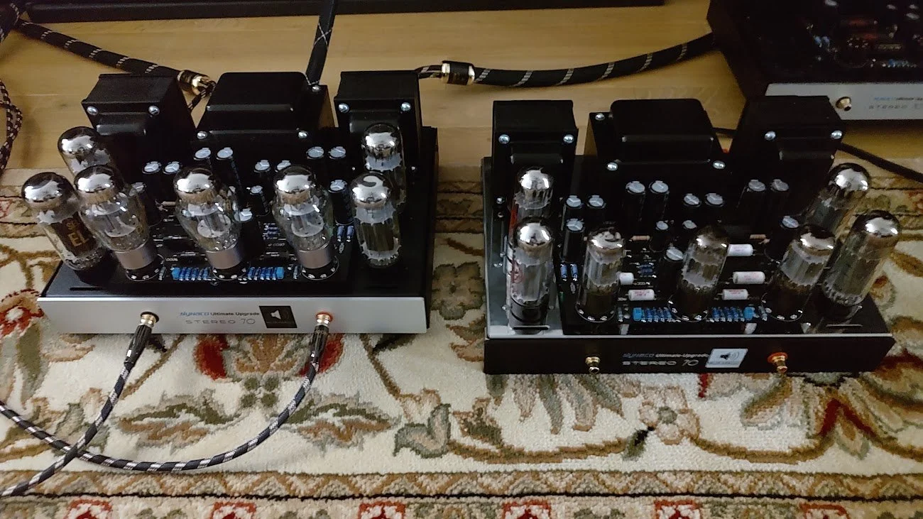 Two tube amplifier heads with vacuum tubes, connected by cables on a patterned rug.