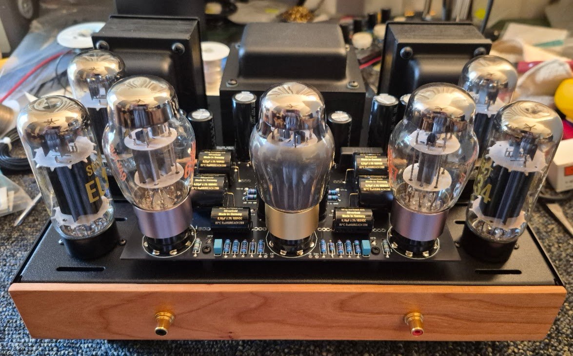 An electronic device with vacuum tubes and electronic components on a black circuit board, mounted on a wooden base.