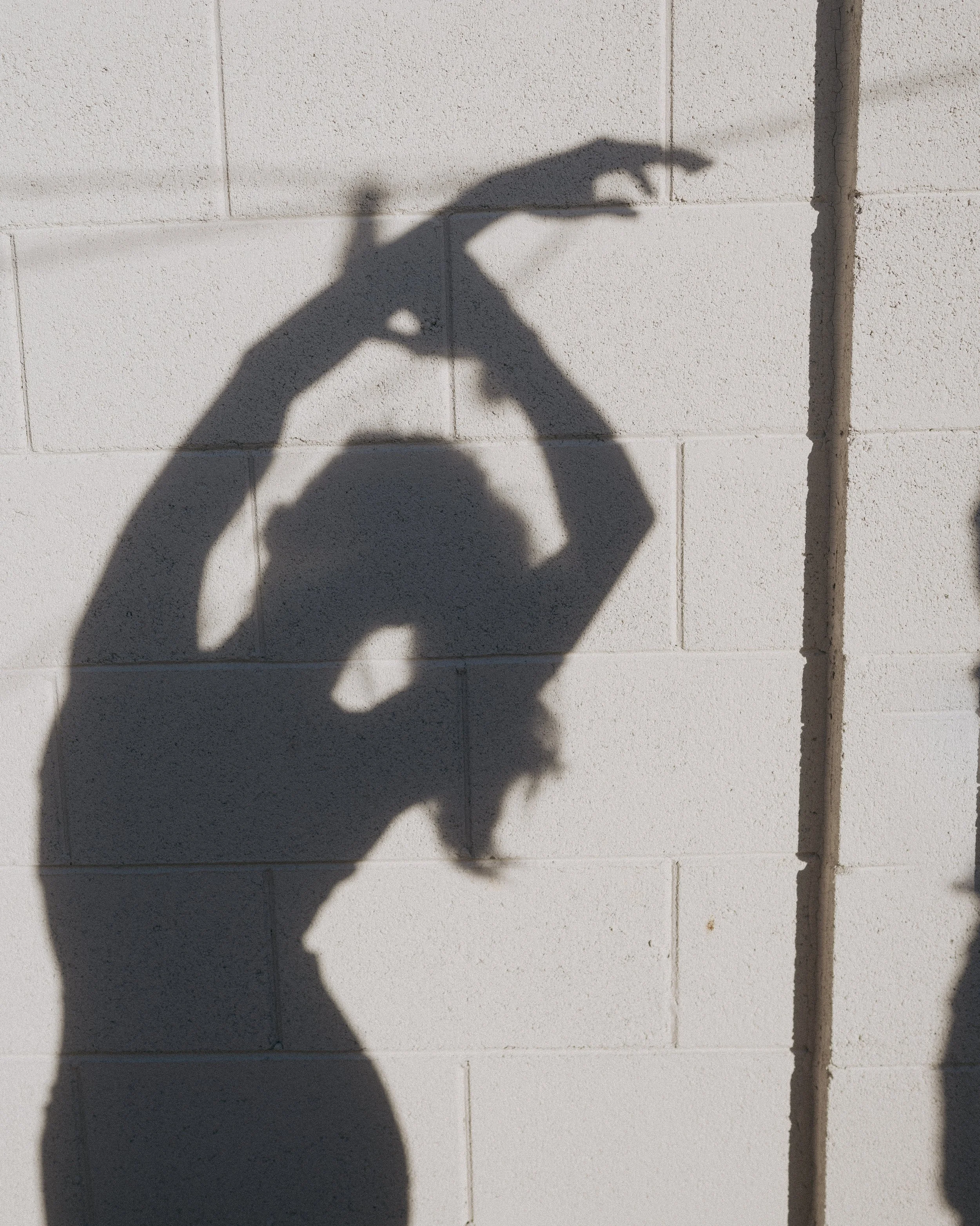 Shadow of a person making a heart shape with their hands on a white brick wall.