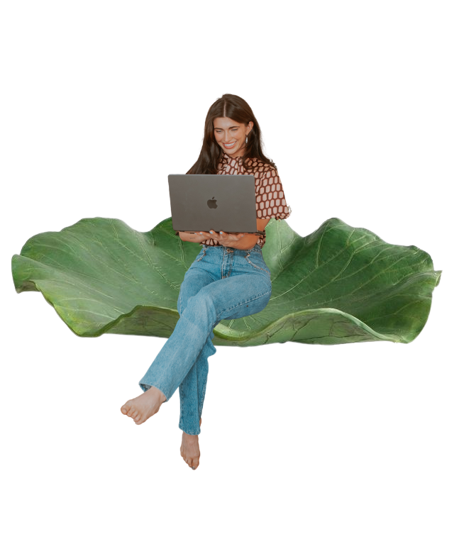 A woman sitting on a large green leaf with a black background, smiling and using a laptop.