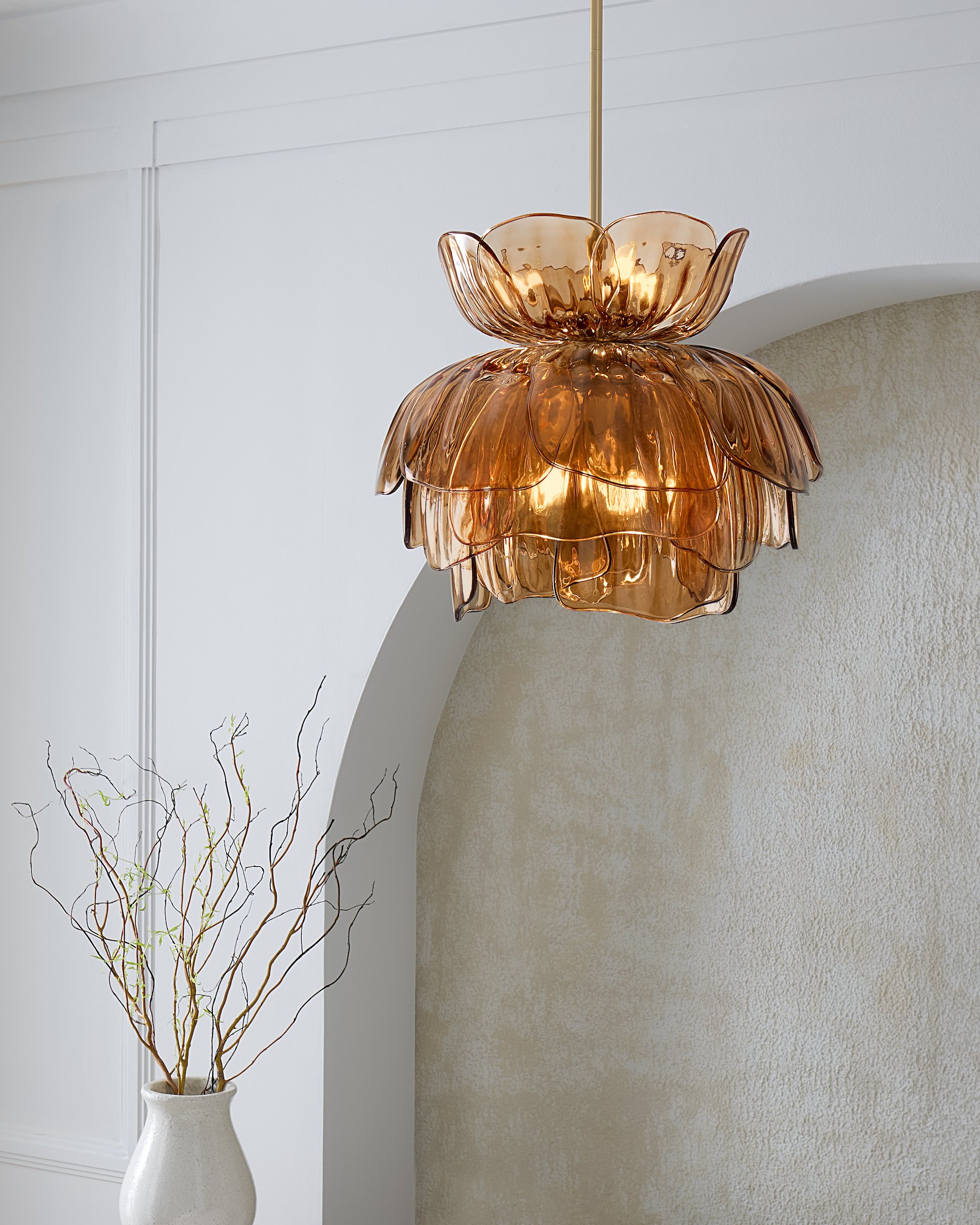 A large, decorative, metallic orange pendant light hanging from the ceiling over a corner of a room. Next to it, there is a tall white ceramic vase with bare, twisting branches.