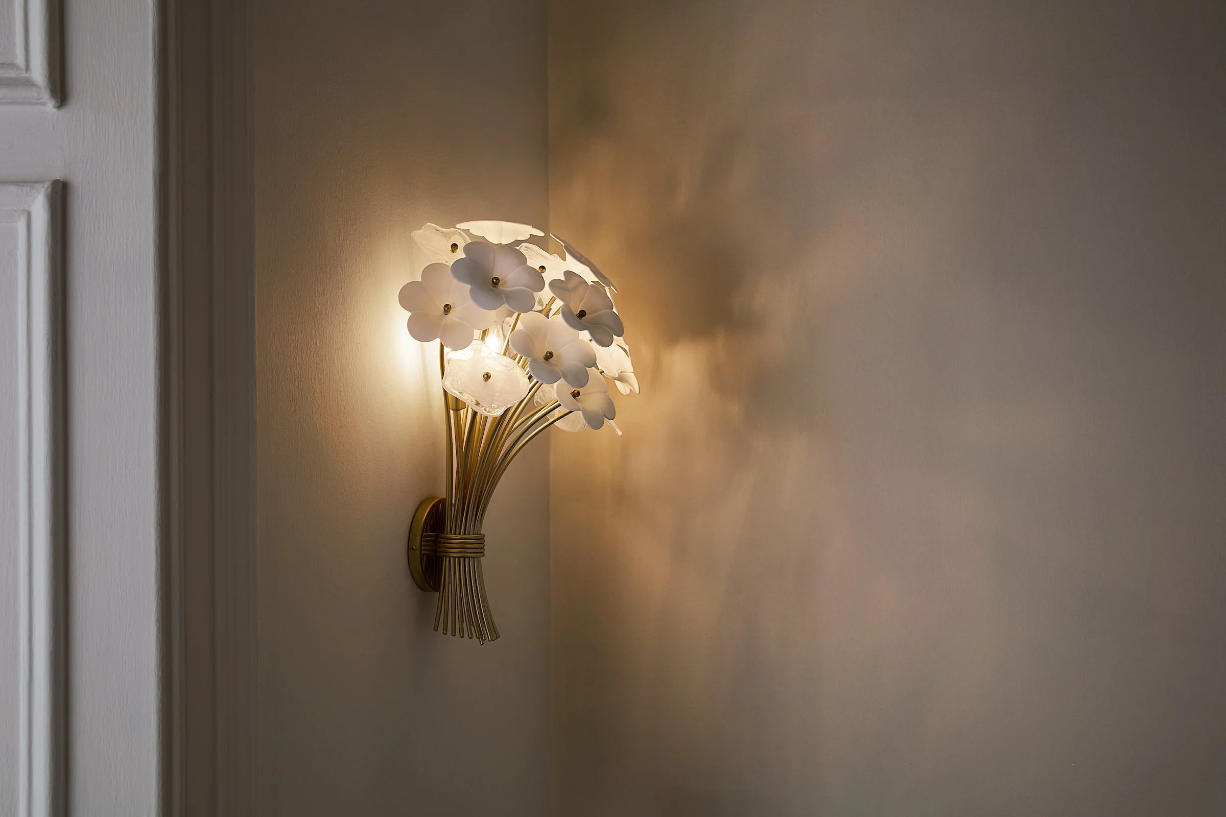 A wall-mounted lamp with white flower-shaped shades casting warm light on a beige wall.