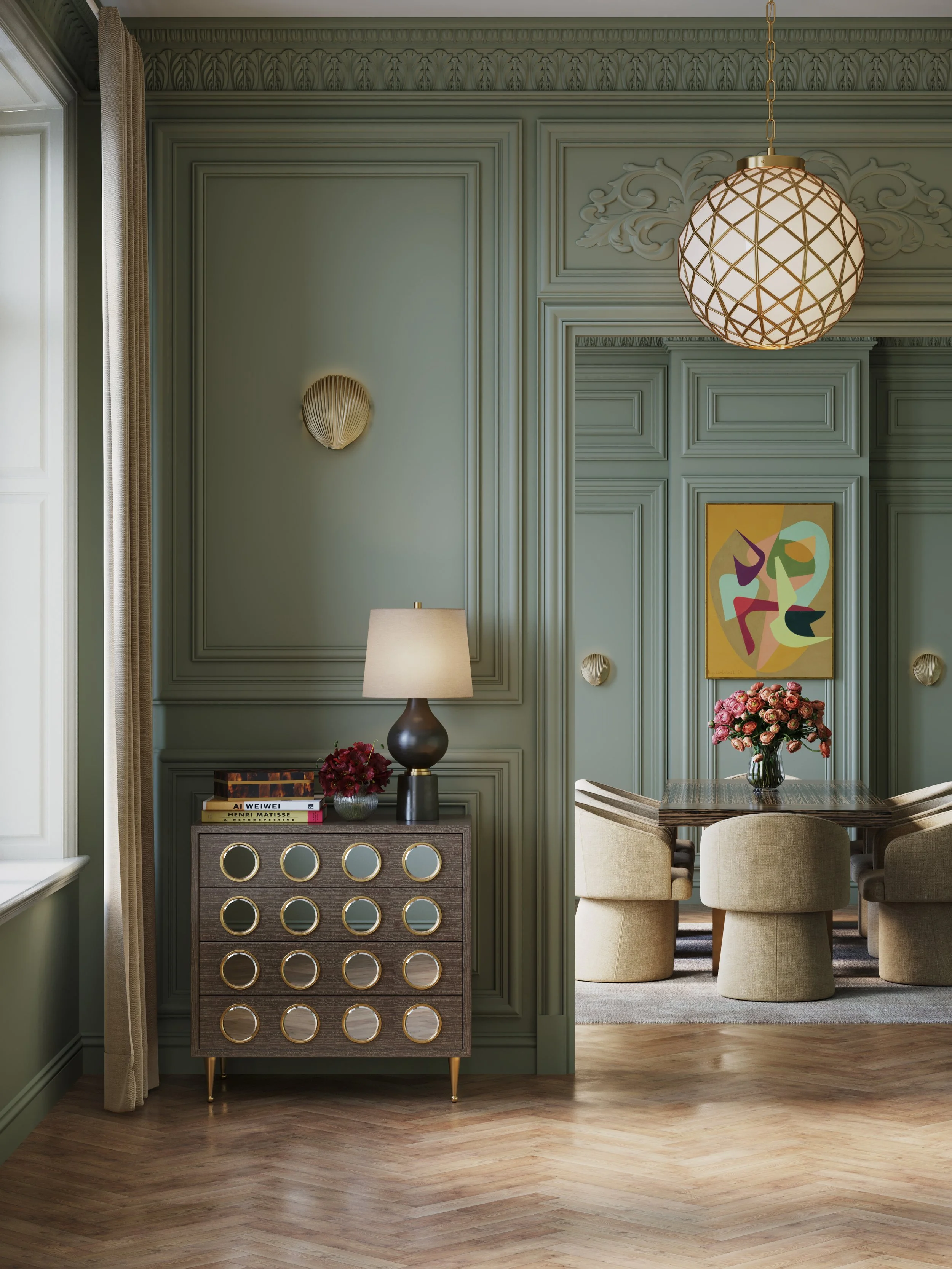 Living room with green paneling on the walls, a black dresser with circular mirror accents, a table lamp, a vase of pink flowers, a colorful abstract painting, and a beige dining table with beige chairs. A large spherical pendant light with a geometric design hangs from the ceiling.