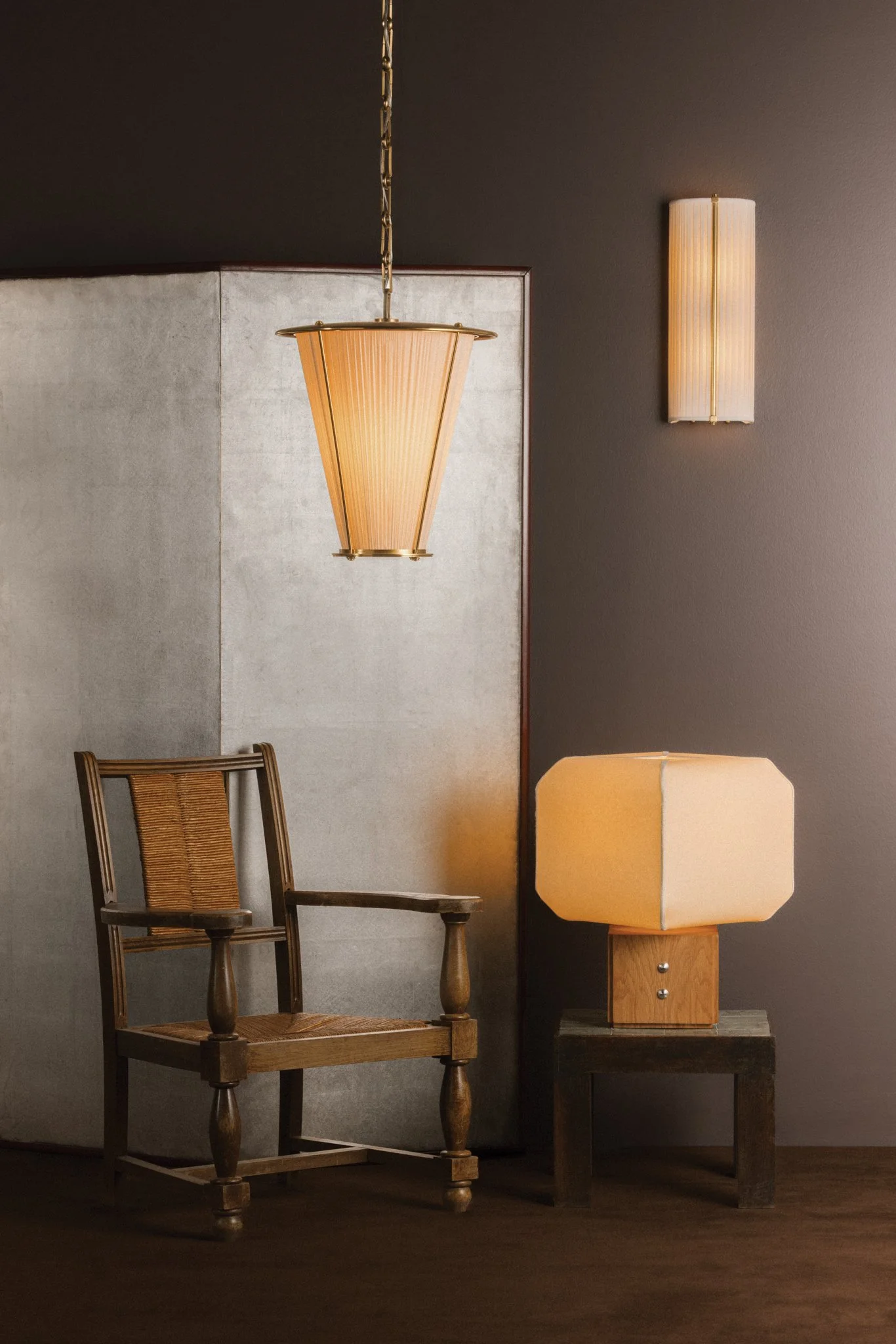 Interior scene with a wooden chair, a table lamp on a small side table, and modern wall-mounted lighting fixtures on a dark wall.