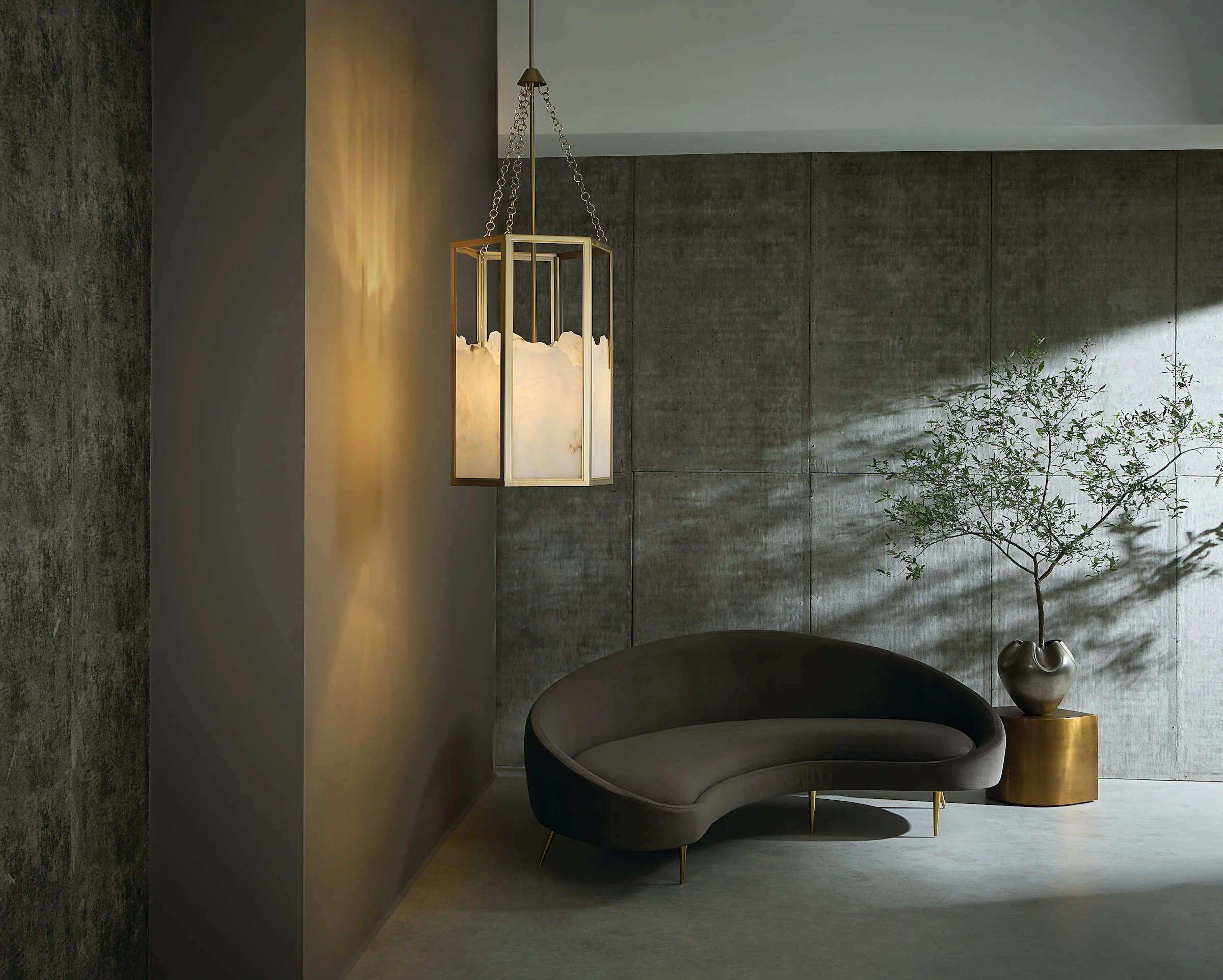 Modern interior room with gray textured concrete walls, a large window with sunlight and shadows, a gray curved armchair, a gold side table with a decorative vase, and a tall hanging lamp with a cloud-like white shade.