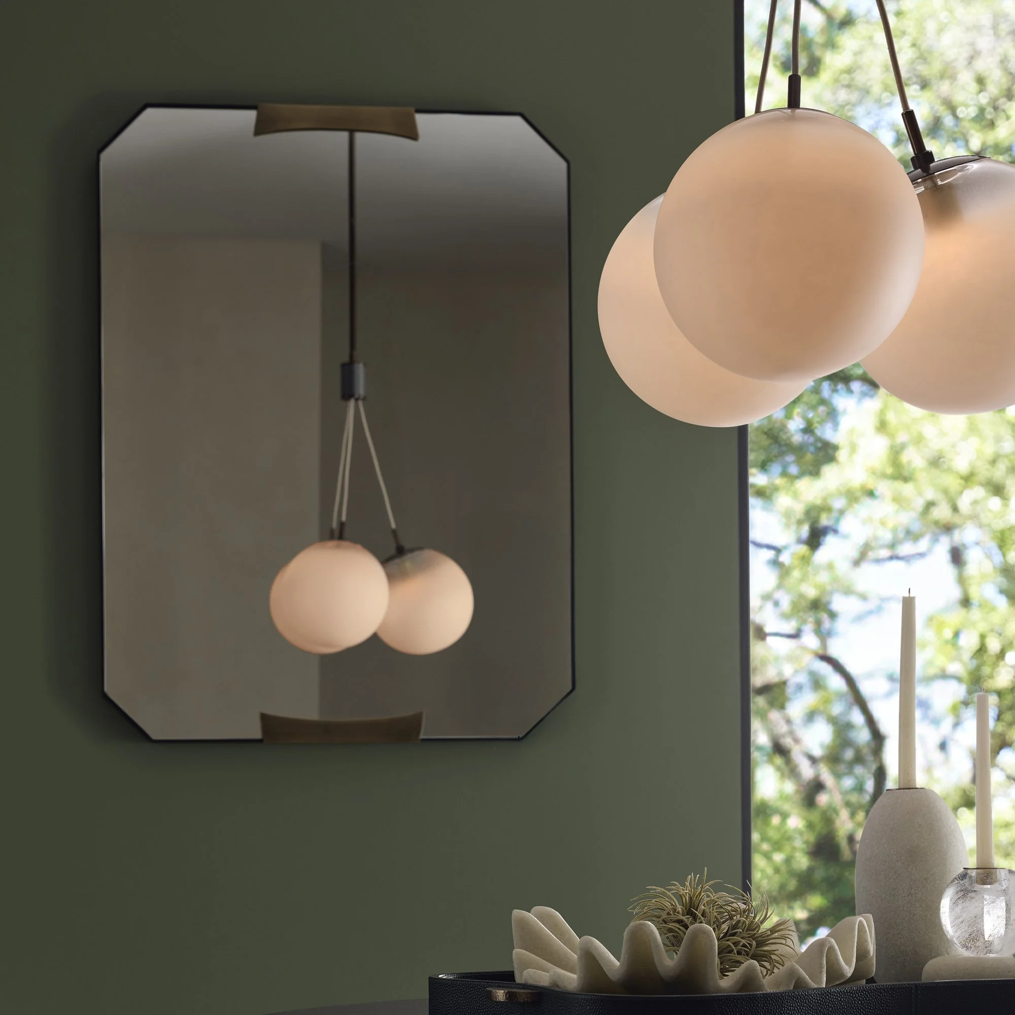 Close-up of modern pendant lights with frosted glass globes hanging in front of a window with trees outside.