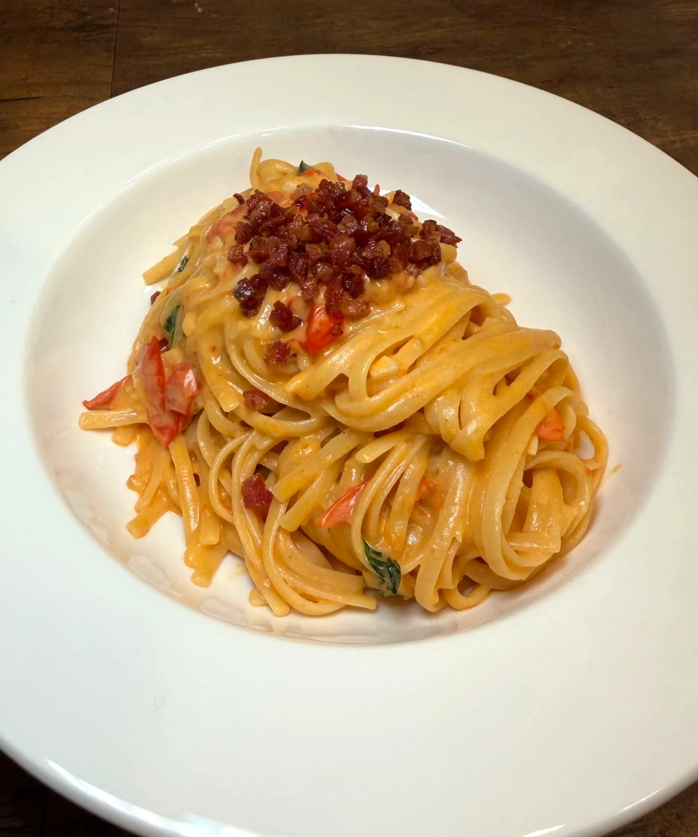 Plate of arrabiata pasta topped with pancetta and garnished with green herbs.