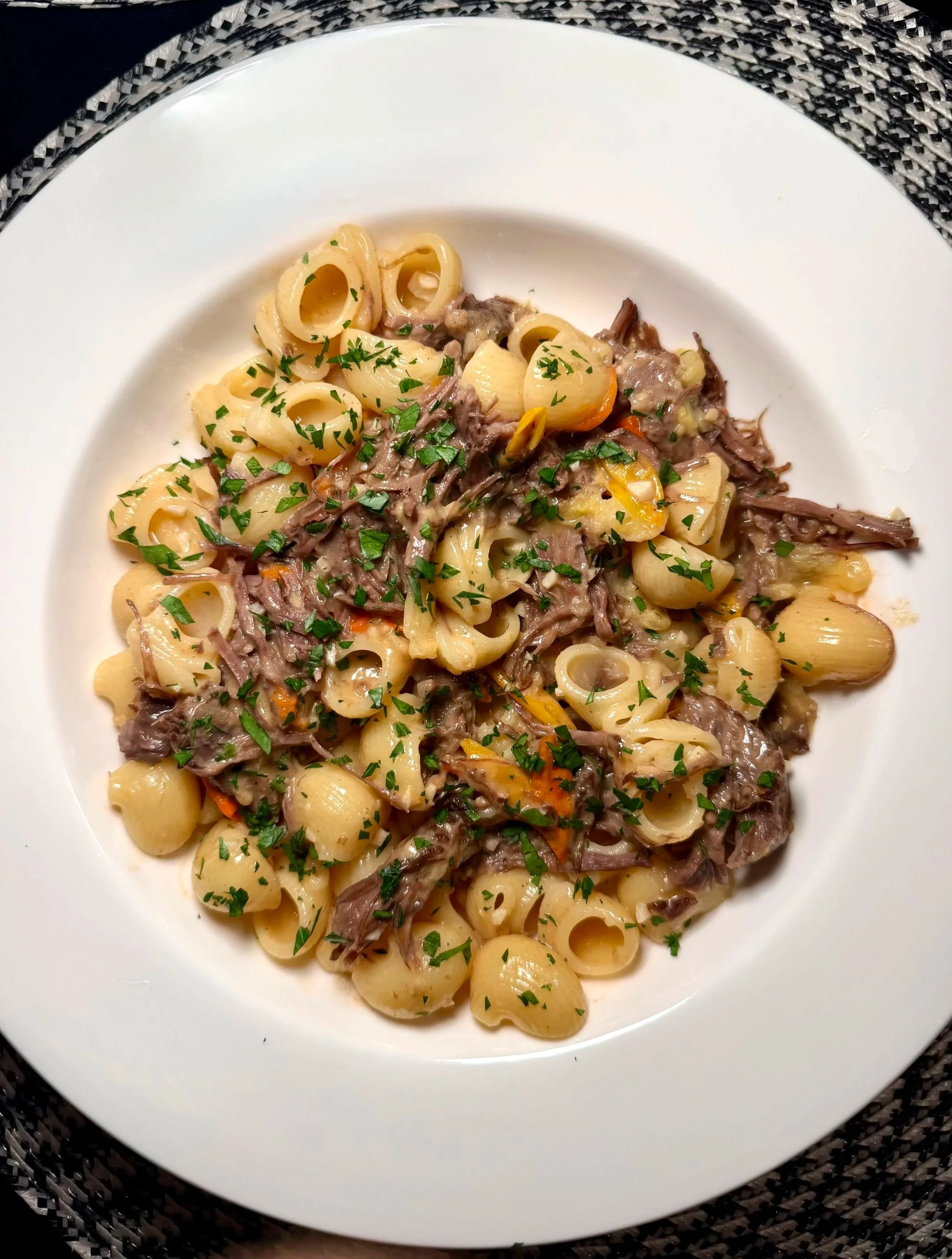 Plate of pasta with shredded beef and chopped parsley garnished, served on a white plate.