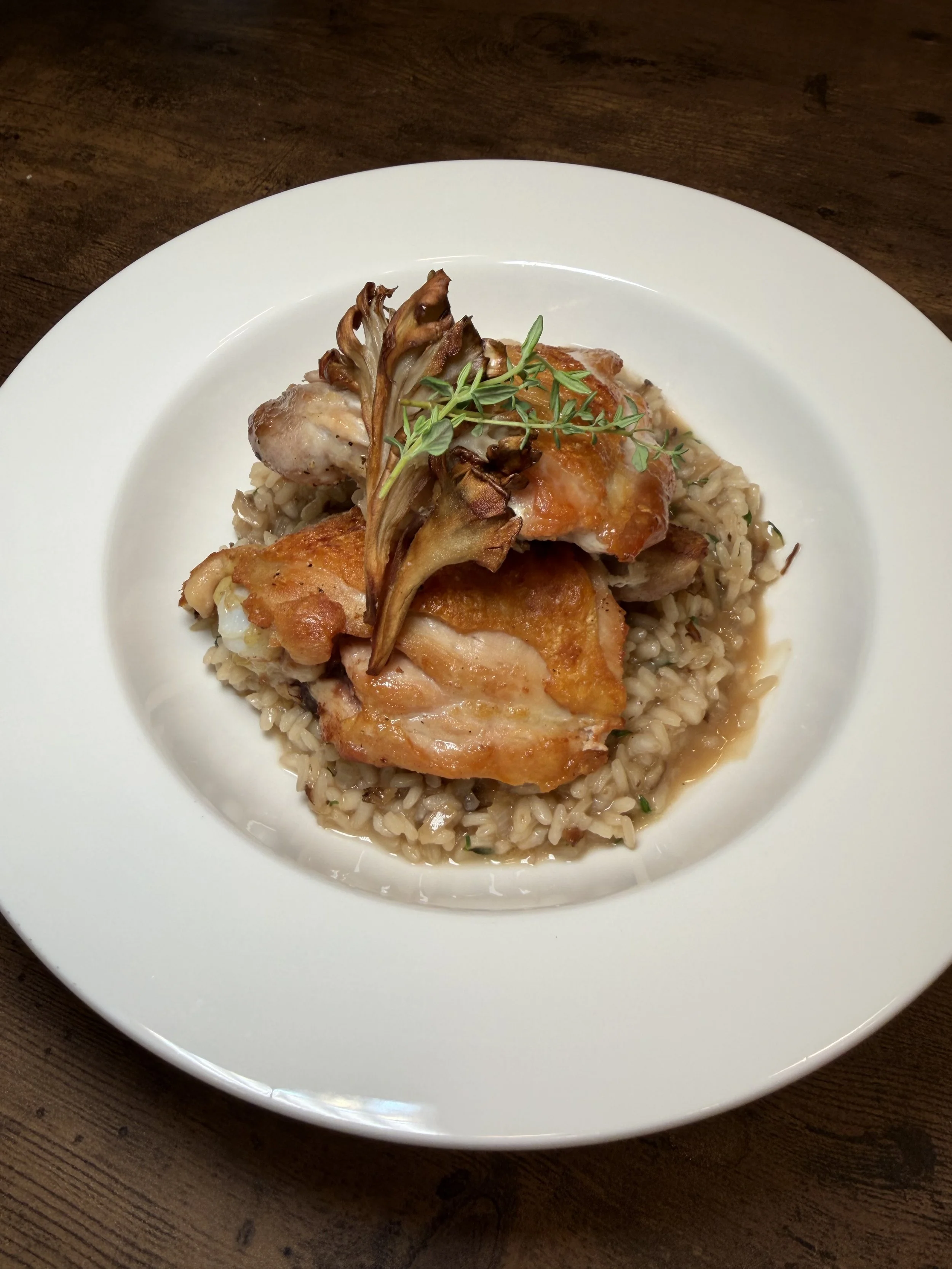 A white plate with cooked rice, topped with roasted chicken, grilled vegetables, and garnished with fresh herbs on a wooden table.
