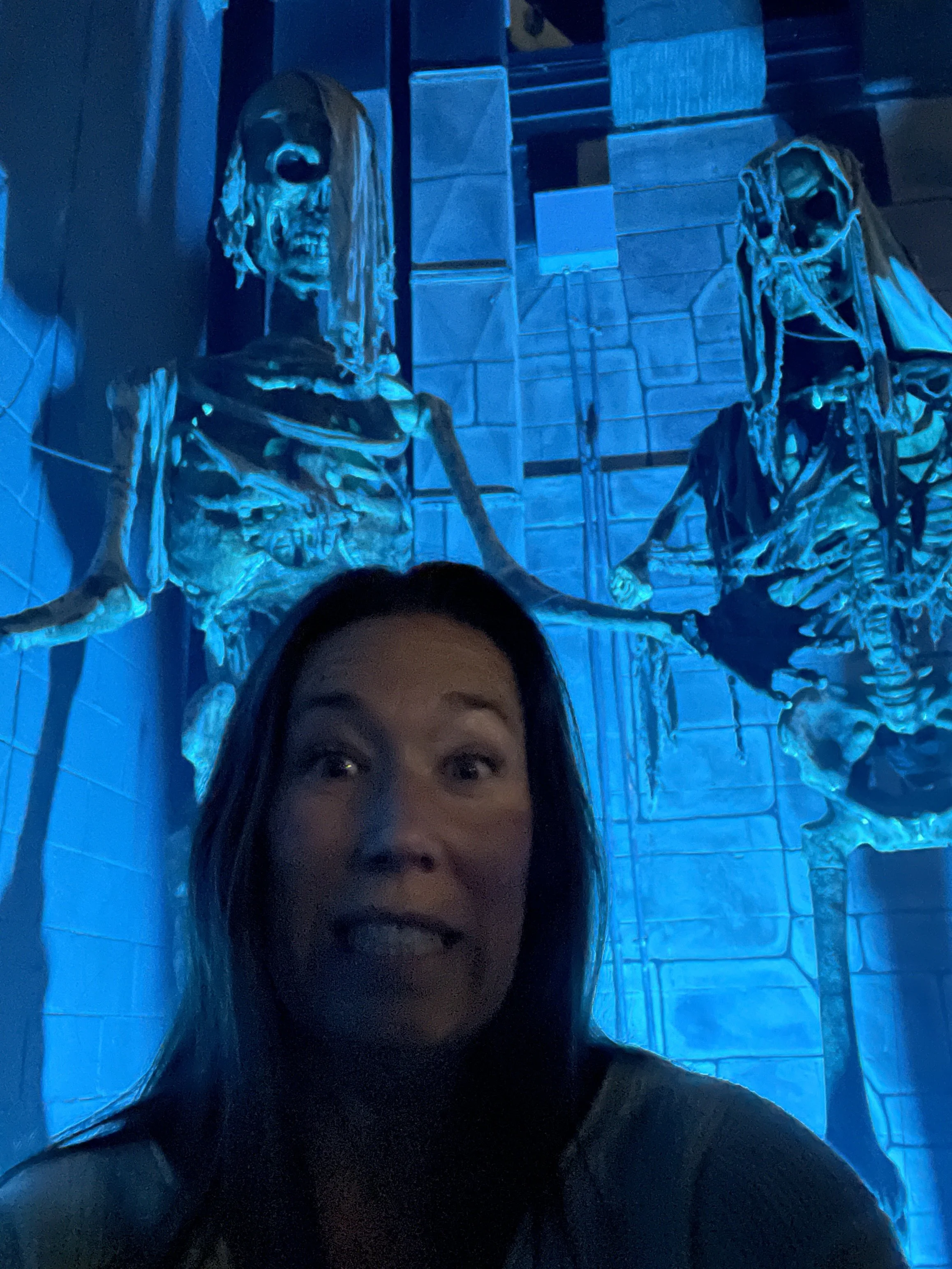 Person taking a selfie in front of metallic skeleton sculptures illuminated by blue lighting.