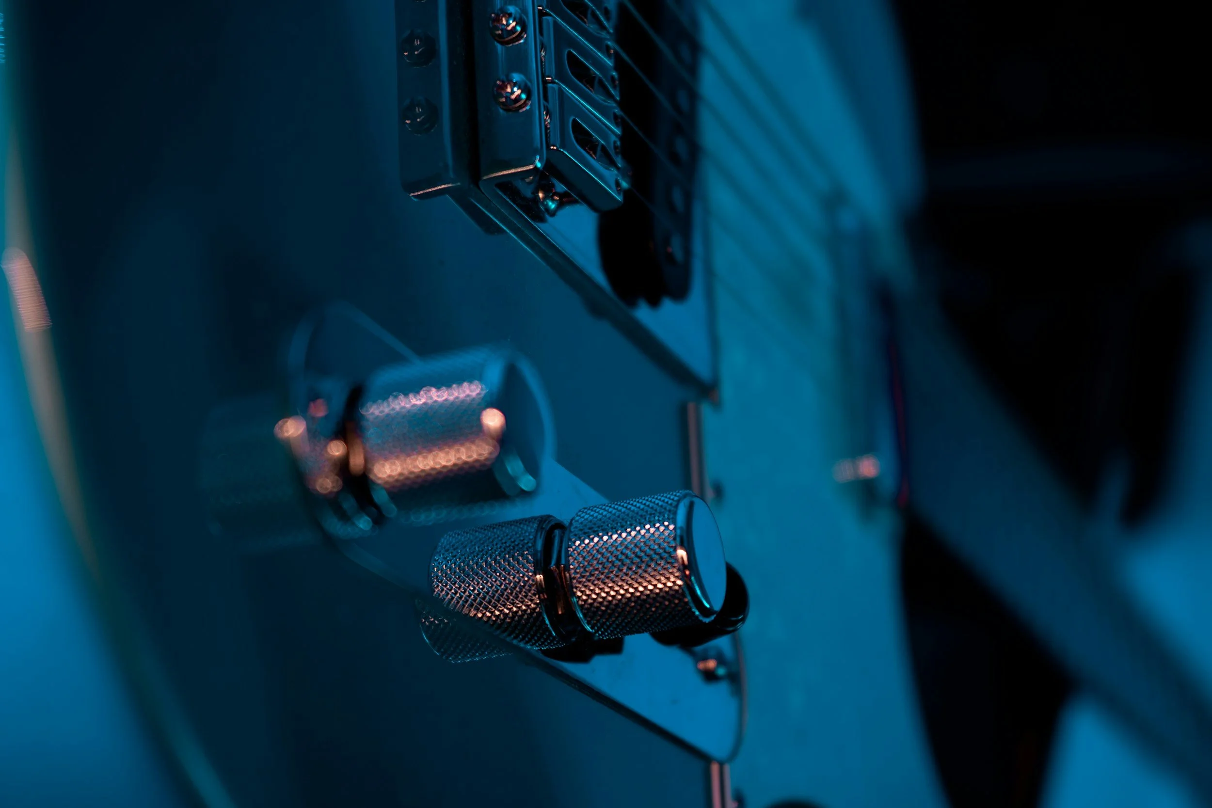 Close-up of a music synthesizer or electronic musical instrument with metallic knobs and connectors, illuminated in blue light.