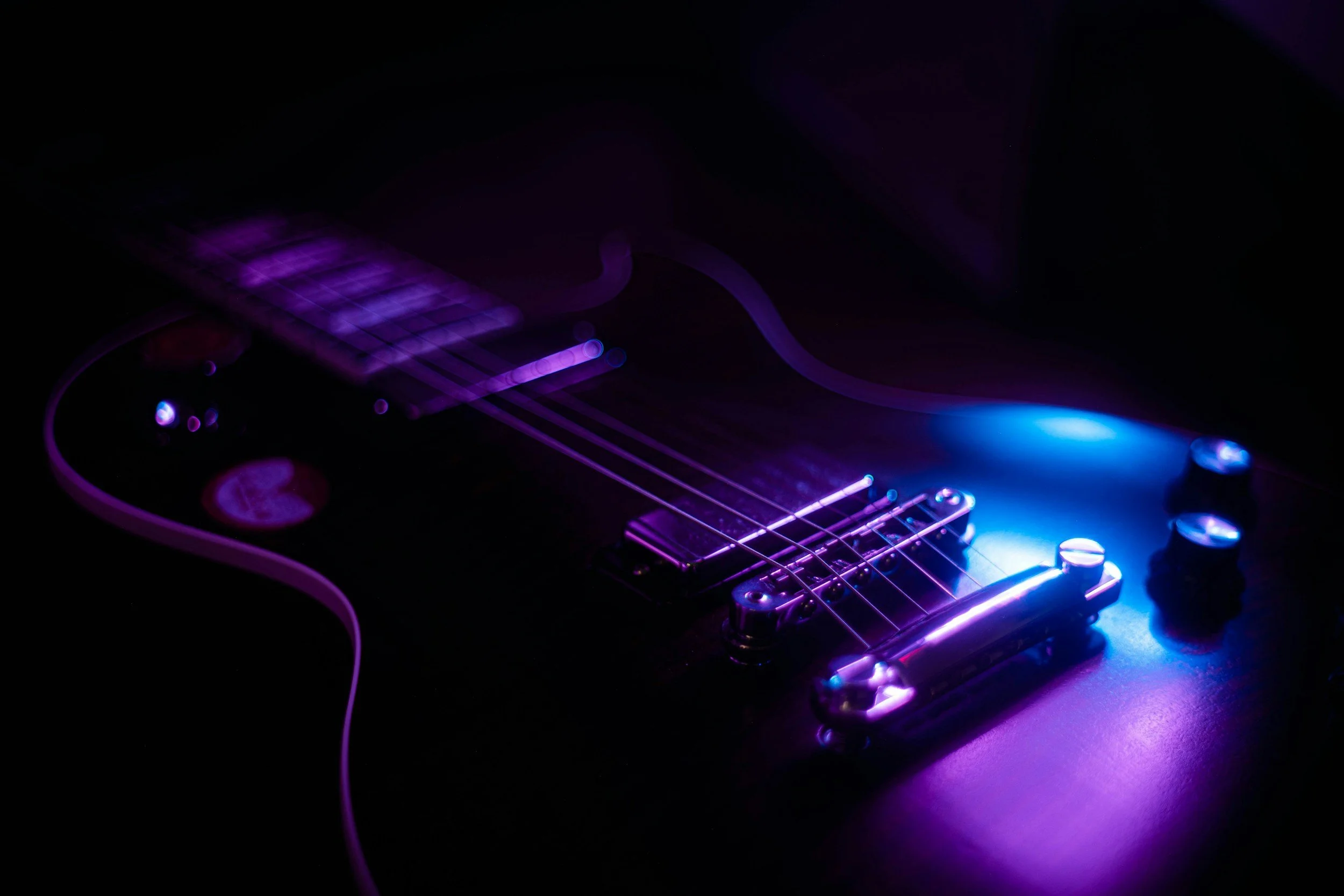 Close-up of an electric guitar with purple and blue lighting effects highlighting the strings and body.