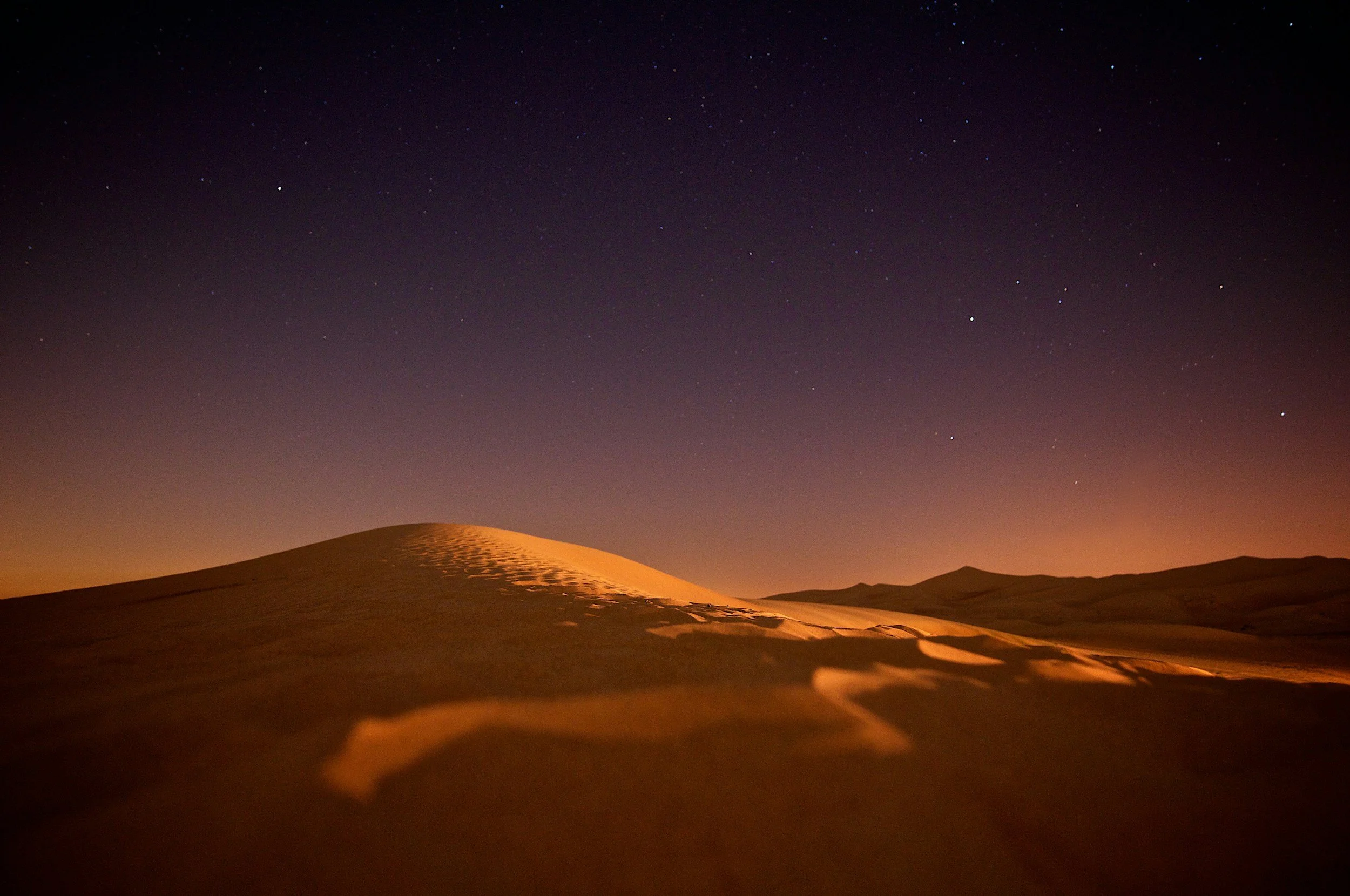 Photo of sand dunes at night with a starry sky above.