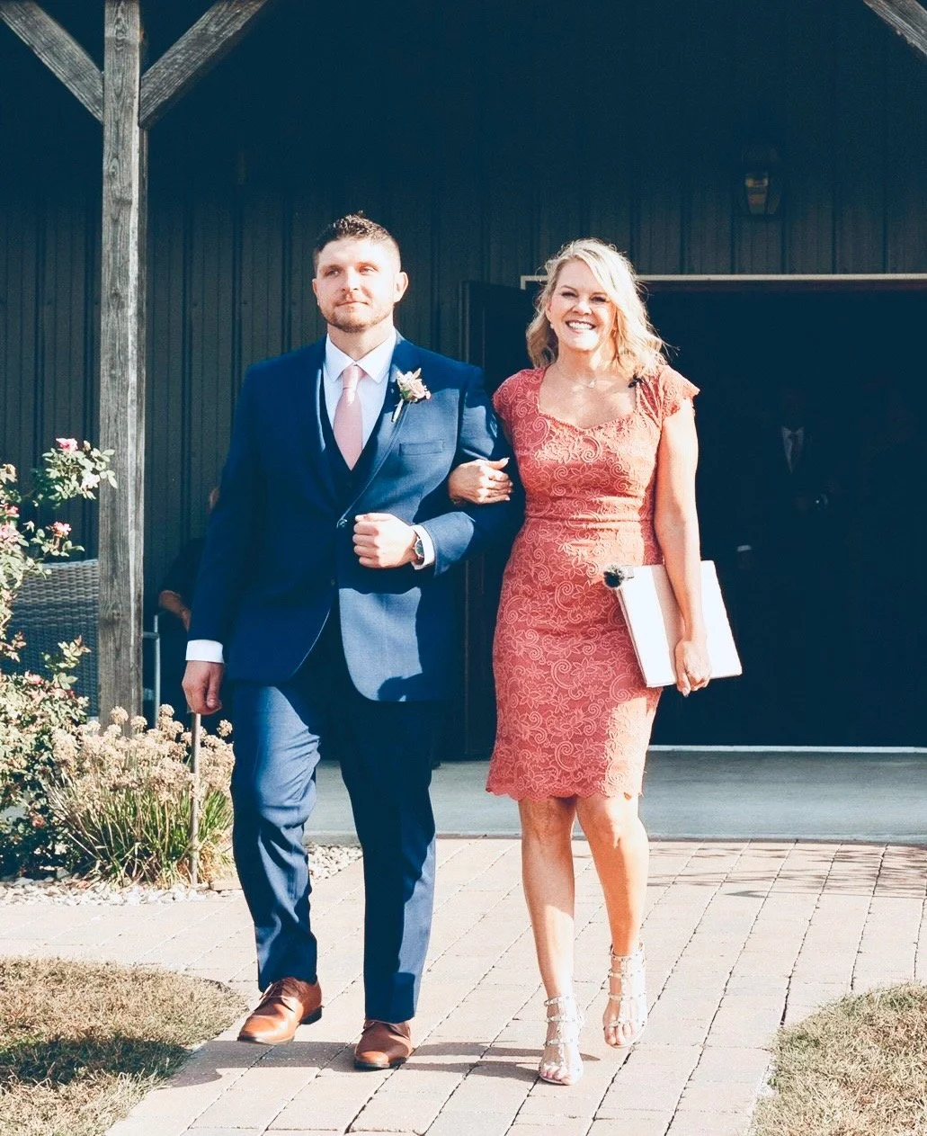 A bride and groom walking arm in arm outdoors, dressed in formal wedding attire, smiling and happy.