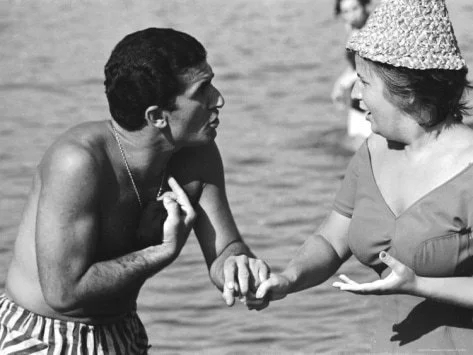 A goofball clowning on an Italian beach. {Black and white photograph depicting a candid, energetic conversation between a man and a woman on a beach}. Photo by Paul Schutzer for LIFE Magazine (Aug. 23, 1963)