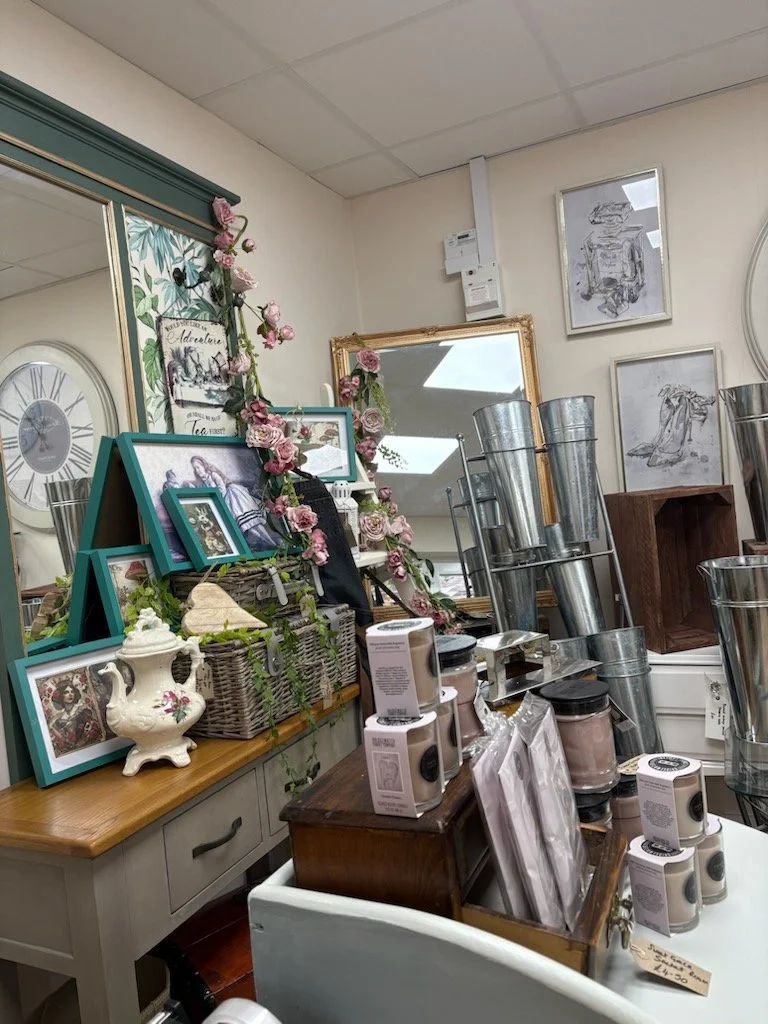 Display of home decor items, including picture frames, floral decorations, vases, and metal buckets, arranged on tables and shelves inside a store.