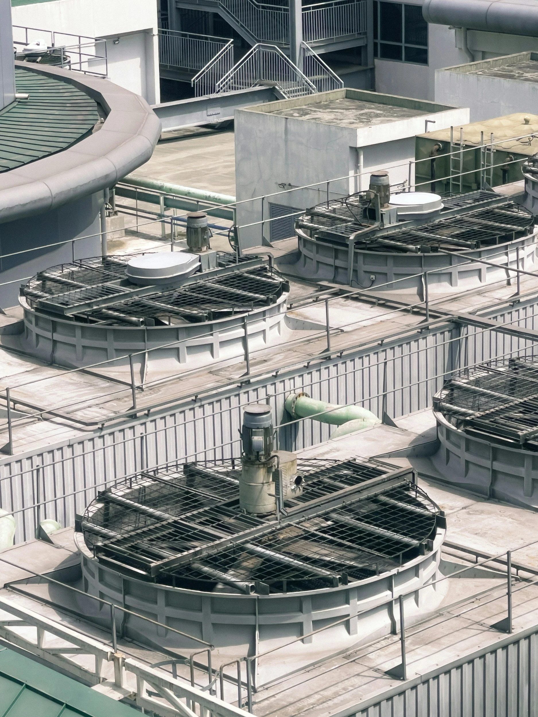 Multiple rooftop air conditioning units and exhaust fans with metal railings on a building rooftop.