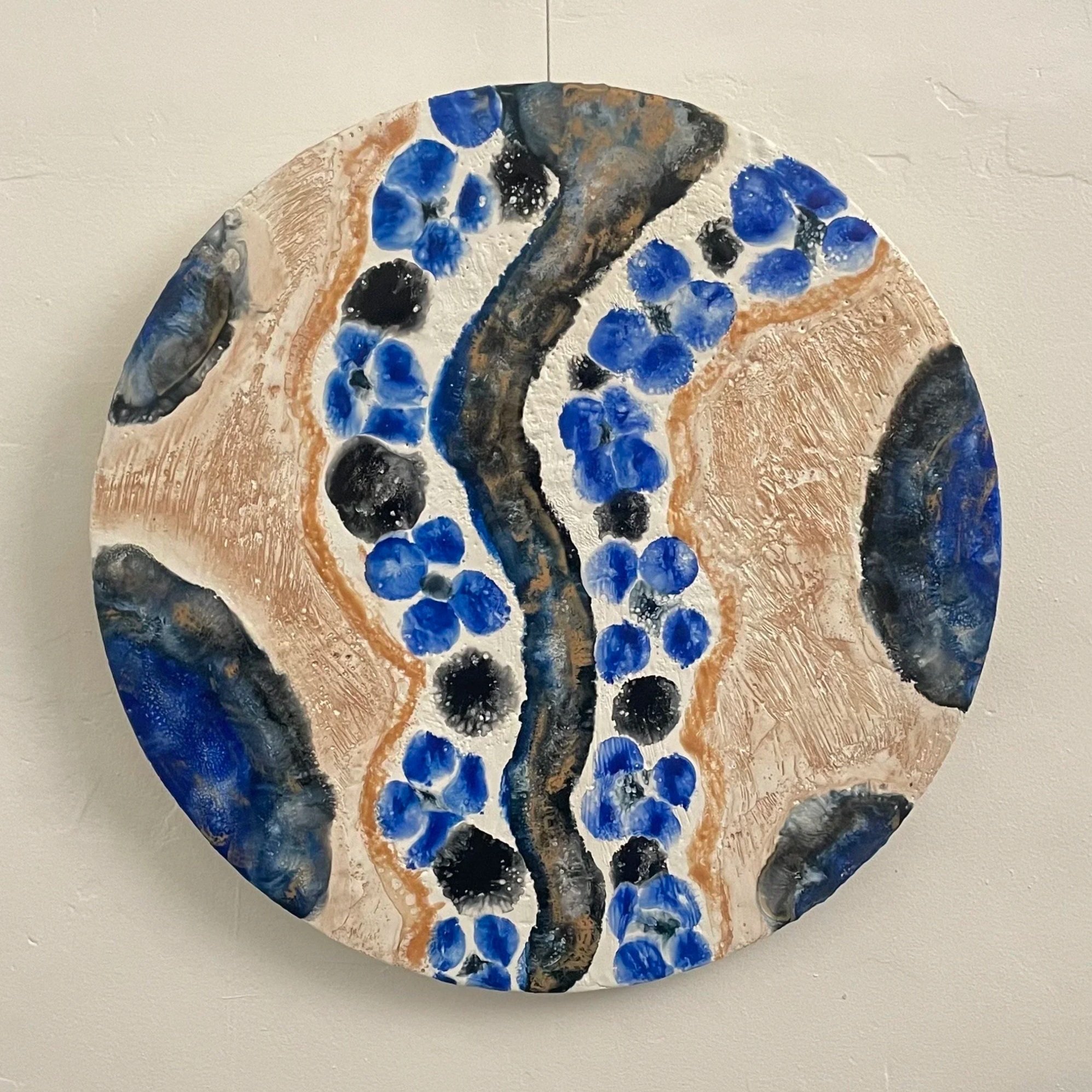 Circular abstract encaustic artwork with gold, blue and black on a white background.