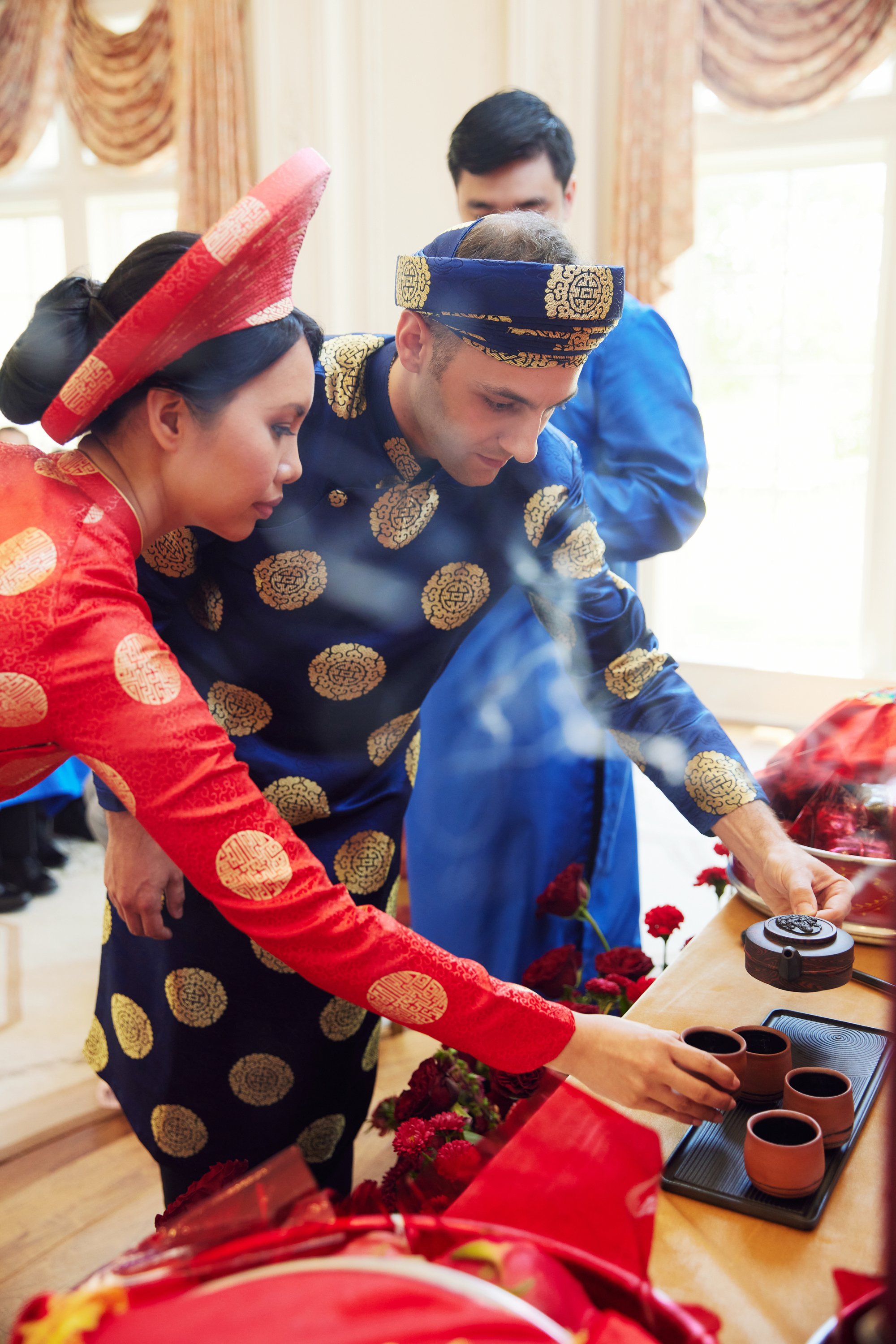 People dressed in traditional Vietnamese clothing participating in a tea ceremony, with cups and flowers on the table.