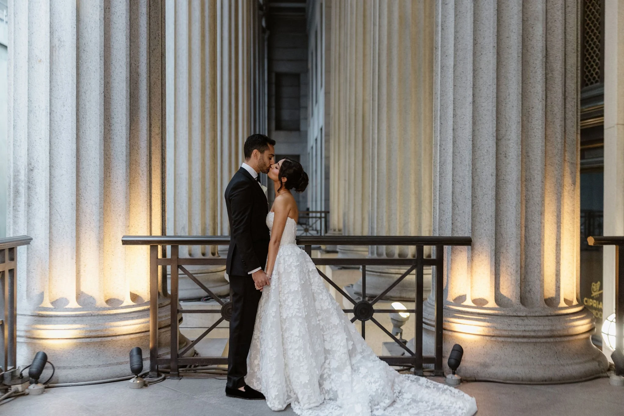 A bride and groom kissing in front of large classical columns at a wedding venue.