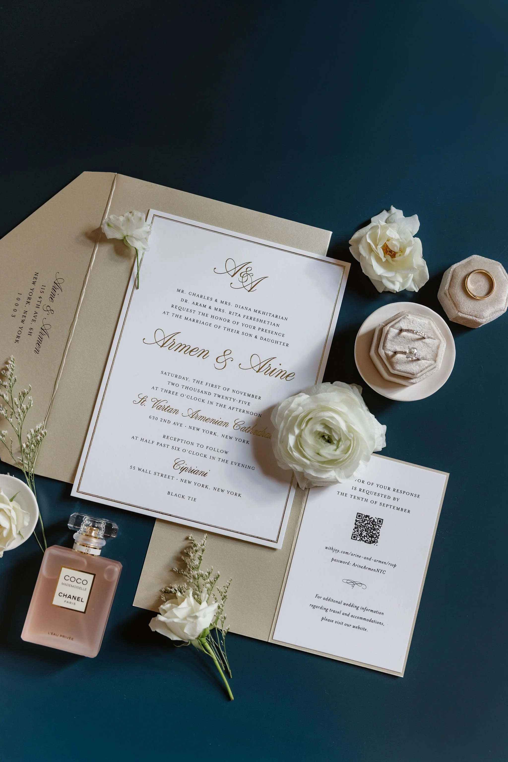 Wedding invitation card with elegant text, white and cream flowers, perfume bottle, and wedding bands on a dark blue background.