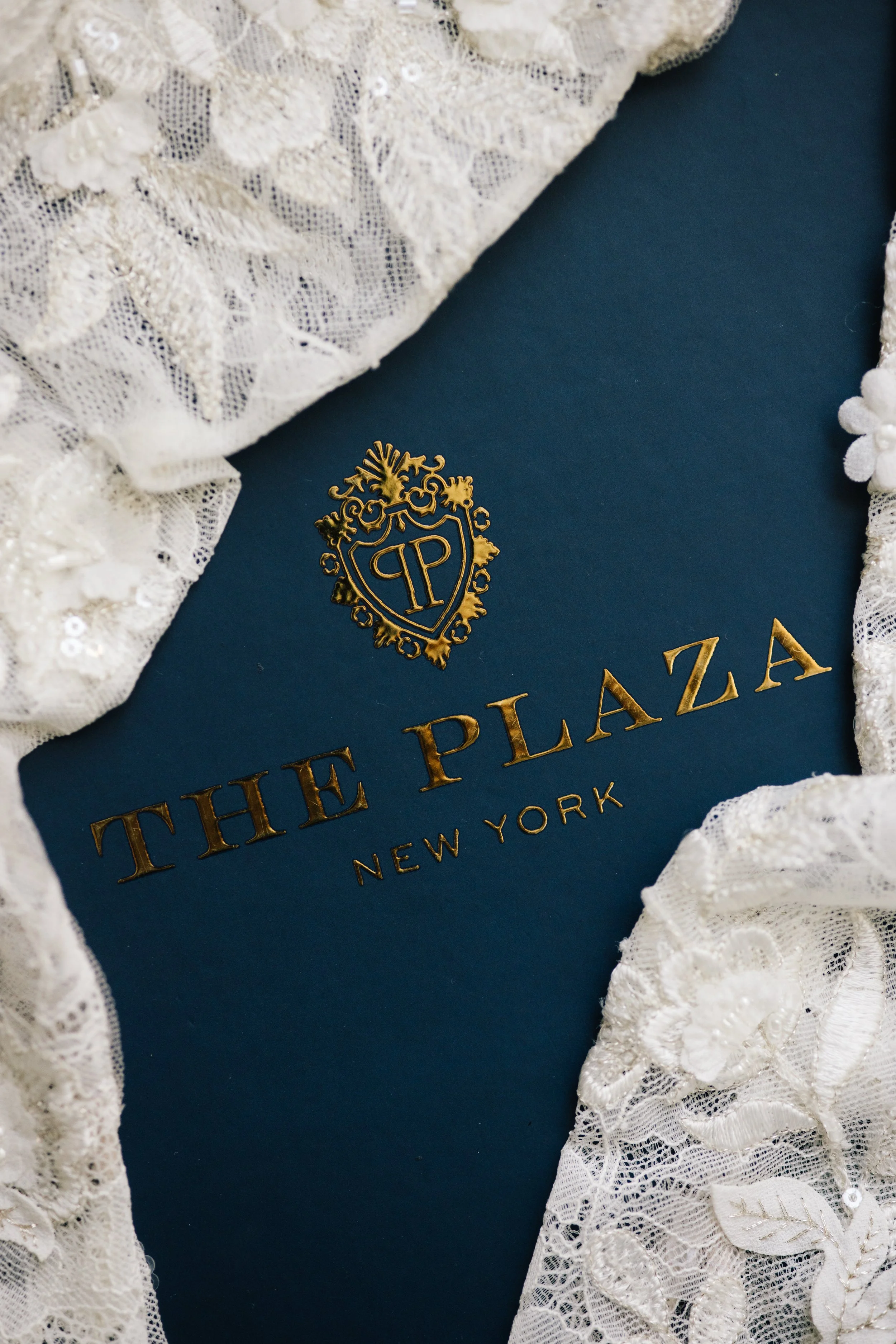 Close-up of a blue book with gold embossed text and a crest, surrounded by white lace fabric.