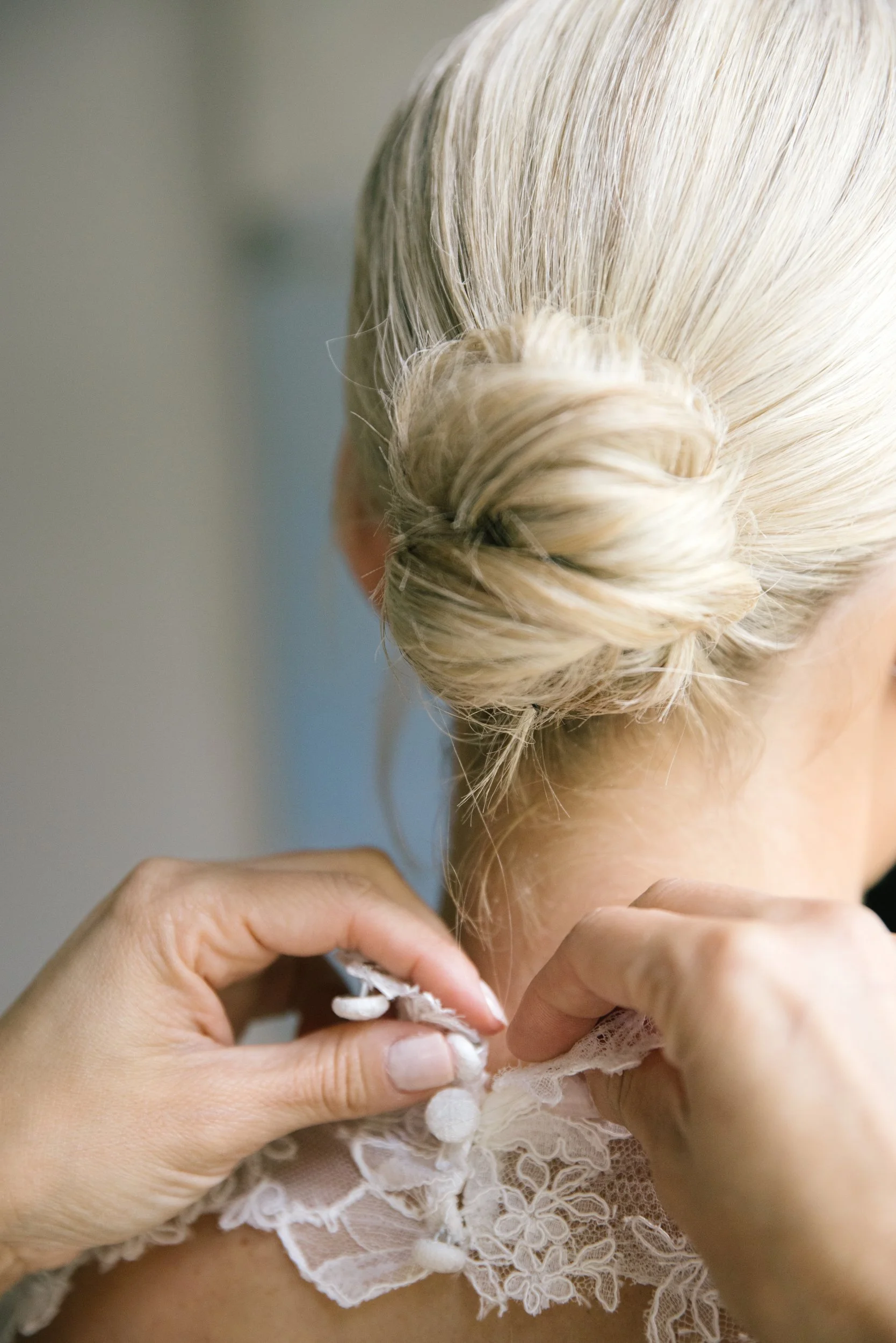 Close-up of a person with platinum blonde hair styled in a twisted bun, wearing a lace garment, and holding a piece of lace fabric.