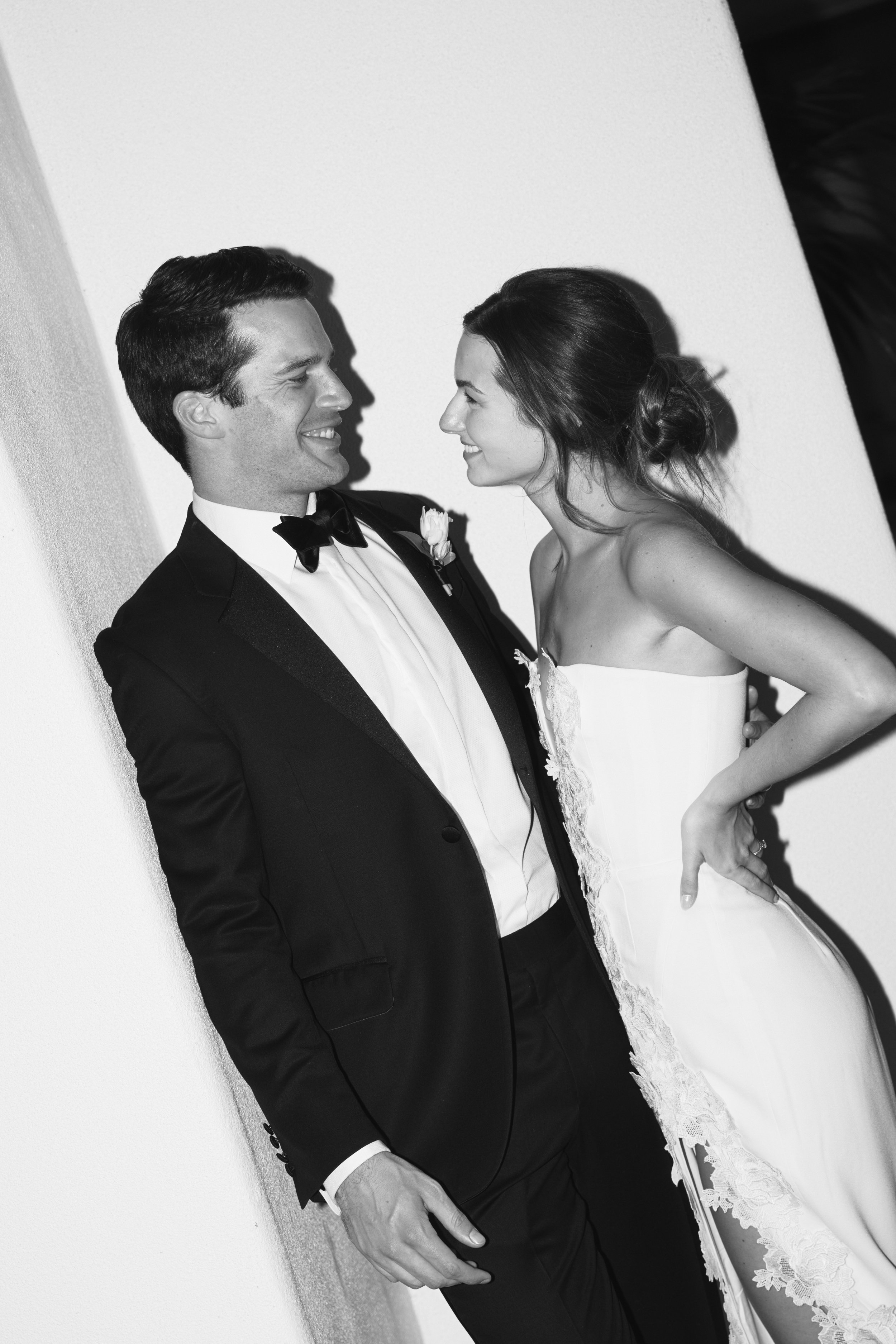 A black and white photo of a smiling man and woman dressed in wedding attire, facing each other close up.