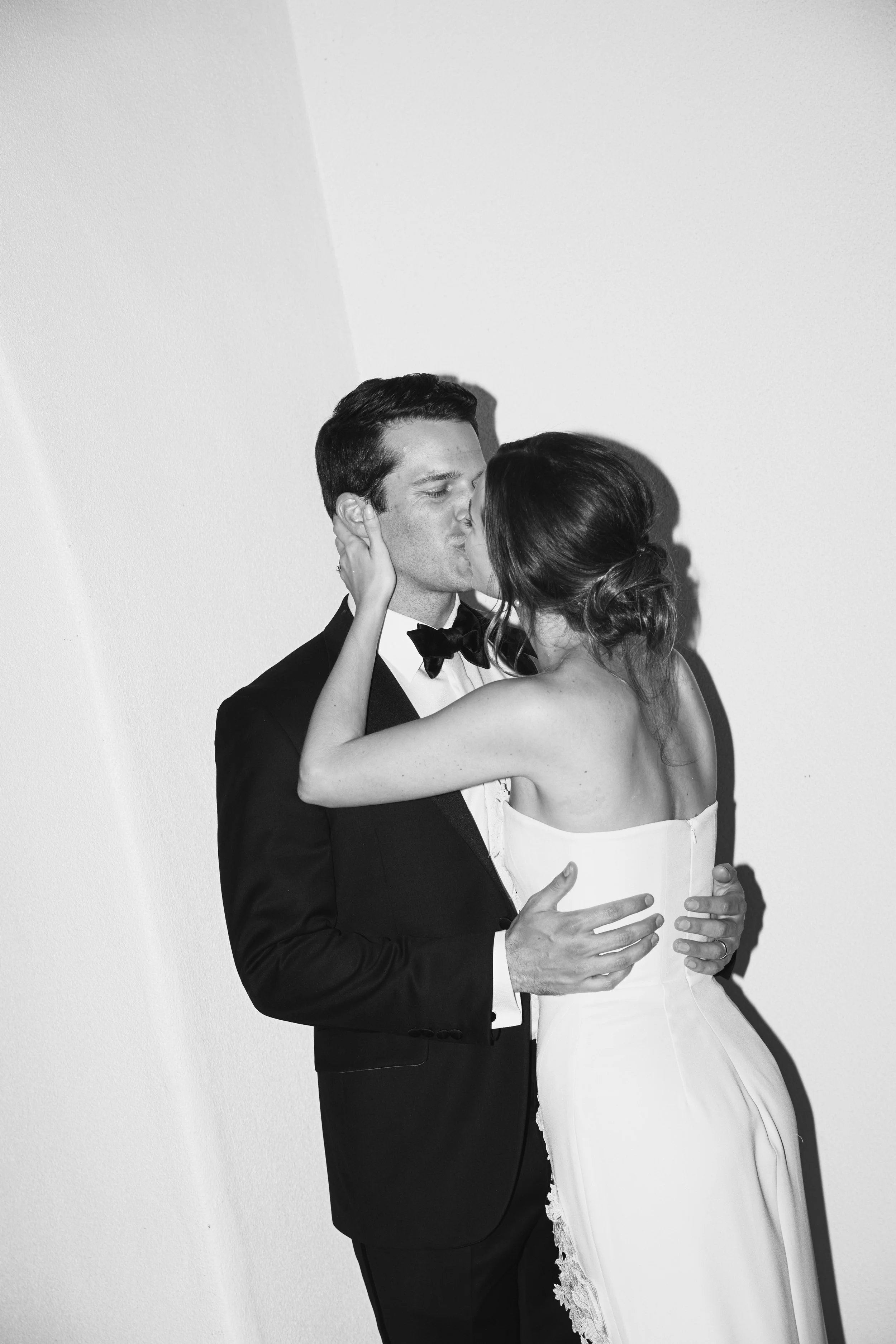 A black and white photo of a bride and groom sharing a kiss and embracing each other.