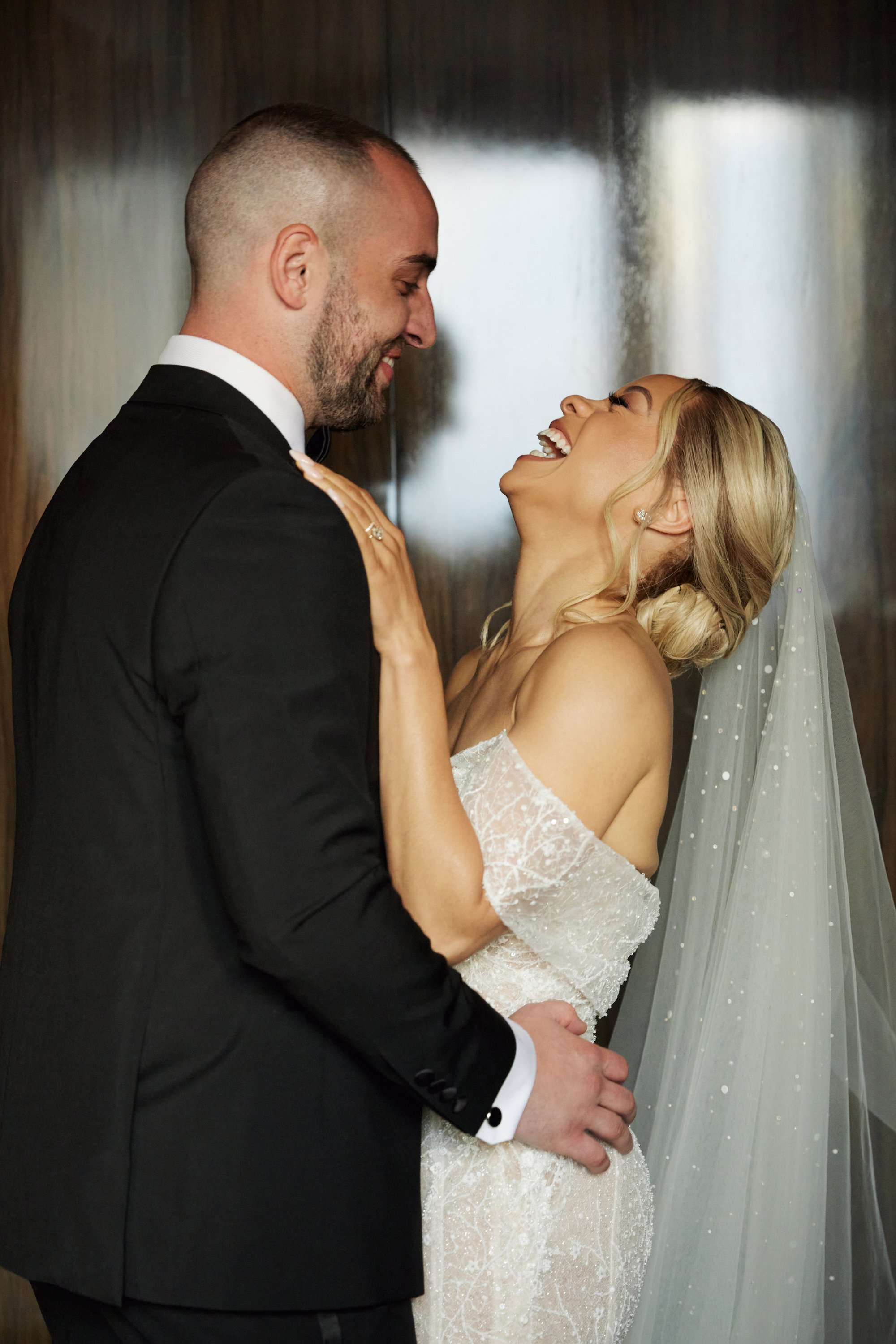 A bride and groom share a joyful moment, looking into each other's eyes and smiling during their wedding.