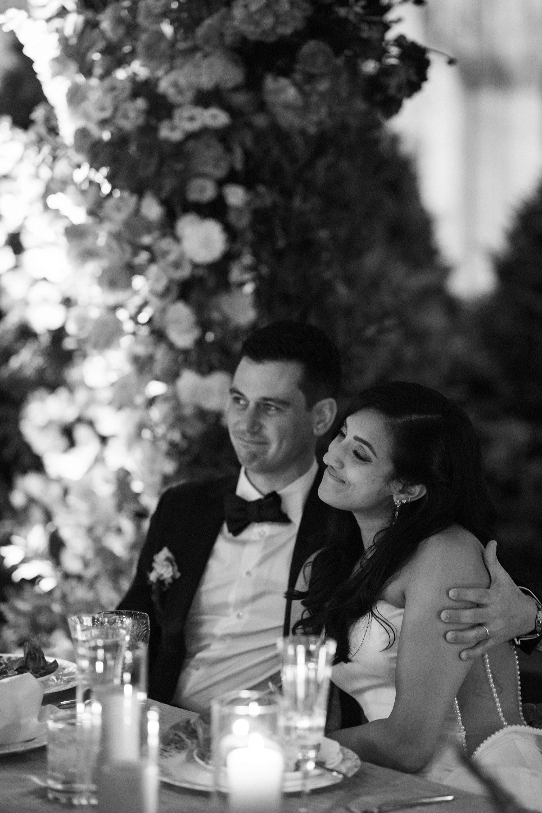 A couple dressed in formal attire seated at a table during a celebration or wedding reception with candles and flowers as decorations.