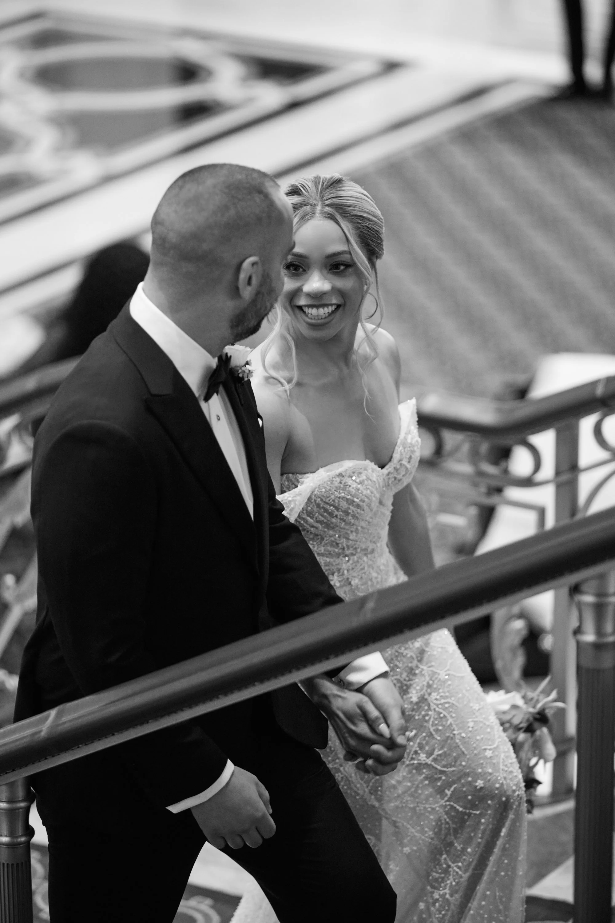 A smiling bride and groom holding hands on a staircase during a wedding celebration.