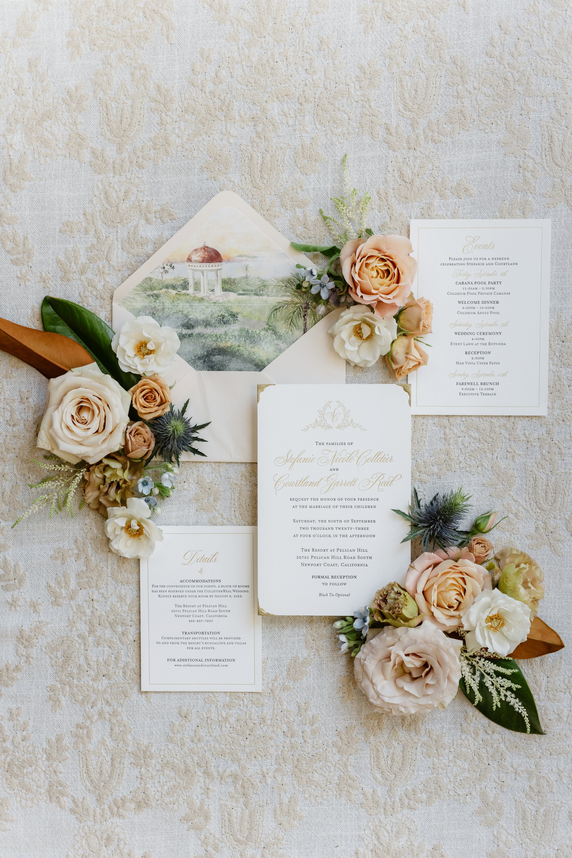 Wedding invitation suite with floral accents and an envelope, laid on a lace tablecloth.