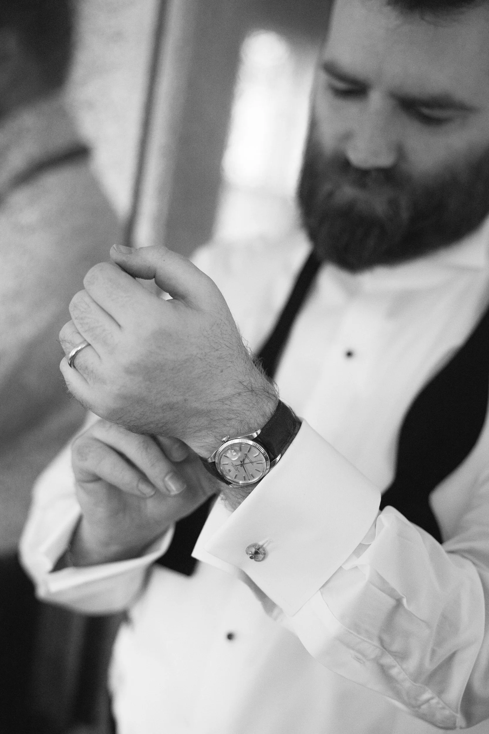Close-up of two men's hands, one with a watch, clasped together during a handshake in a professional setting. One man is wearing a white shirt with cufflinks, while the other is in a dark suit. Part of their faces are visible, with one man sporting a