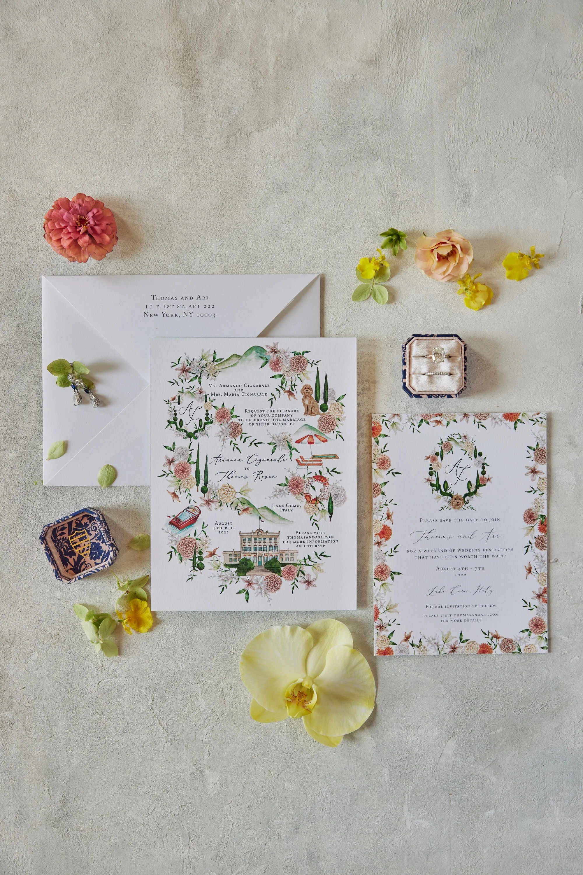 Wedding invitation stationery with floral illustrations, an envelope addressed to Thomas and Ari, and a wedding map of Lake Como, Italy, decorated with flowers and petals.