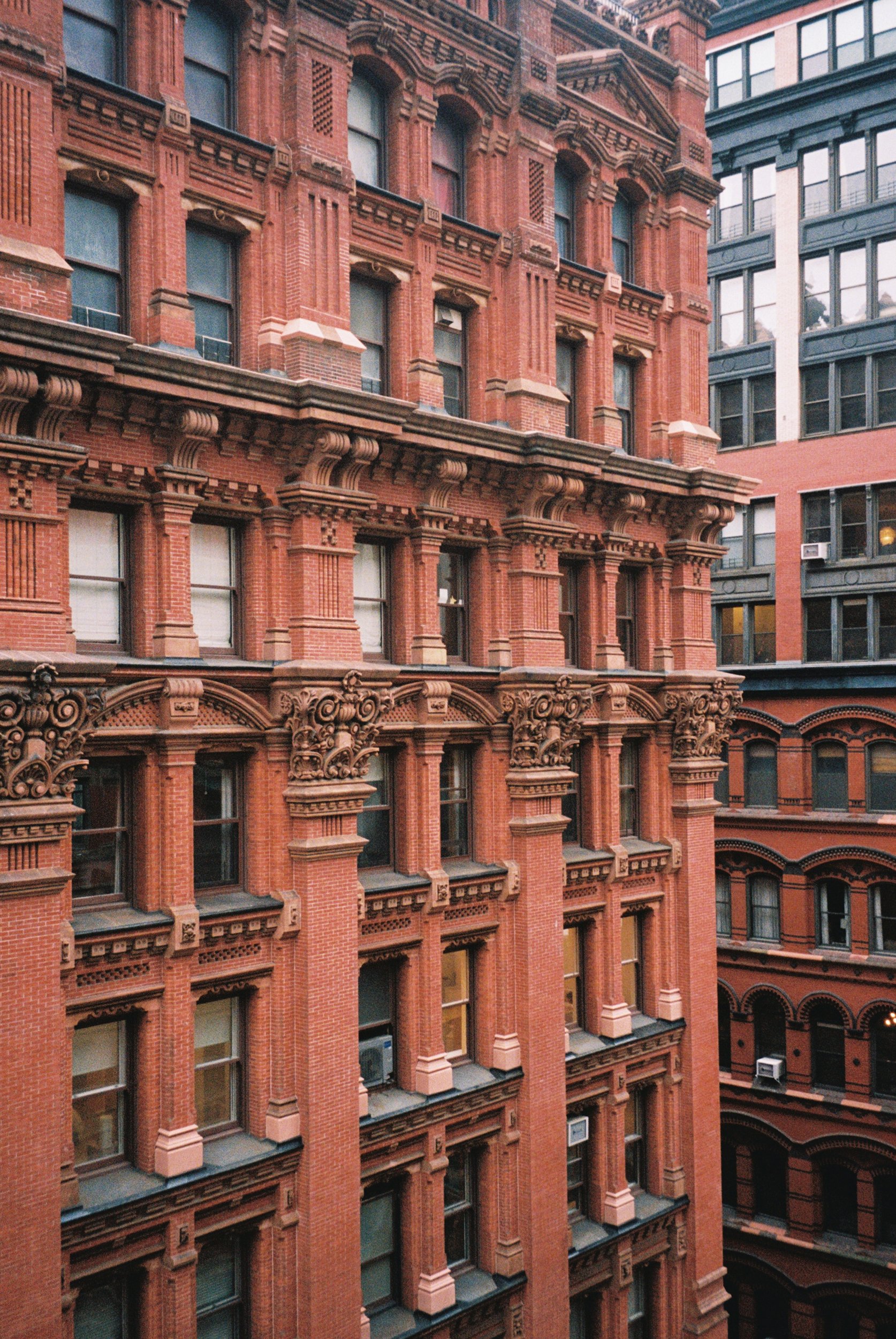A close-up view of a historic red brick building with ornate architectural details, multiple windows, and fire escapes.