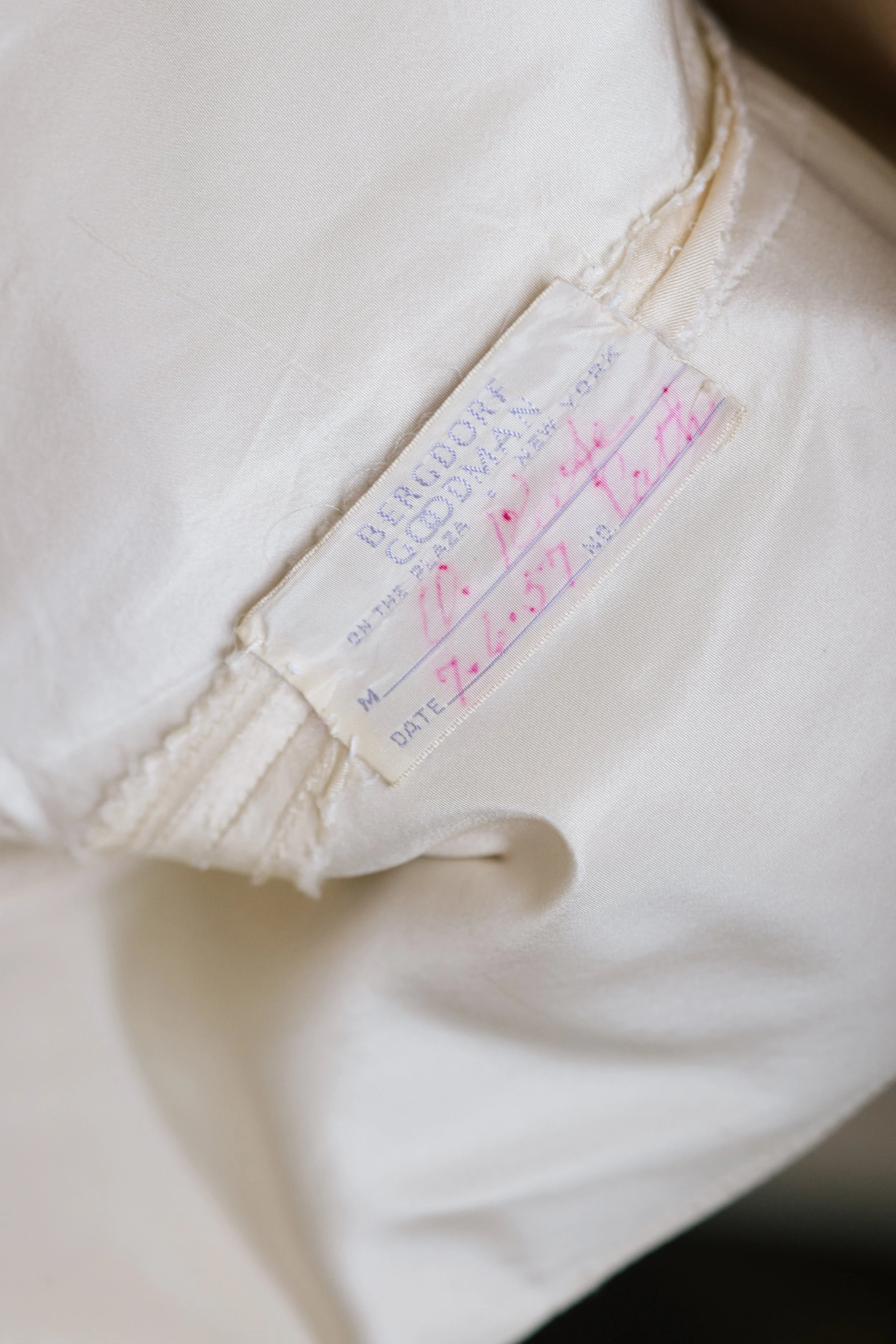 Close-up of a white fabric label sewn inside a cream-colored garment, showing faded writing and signatures.