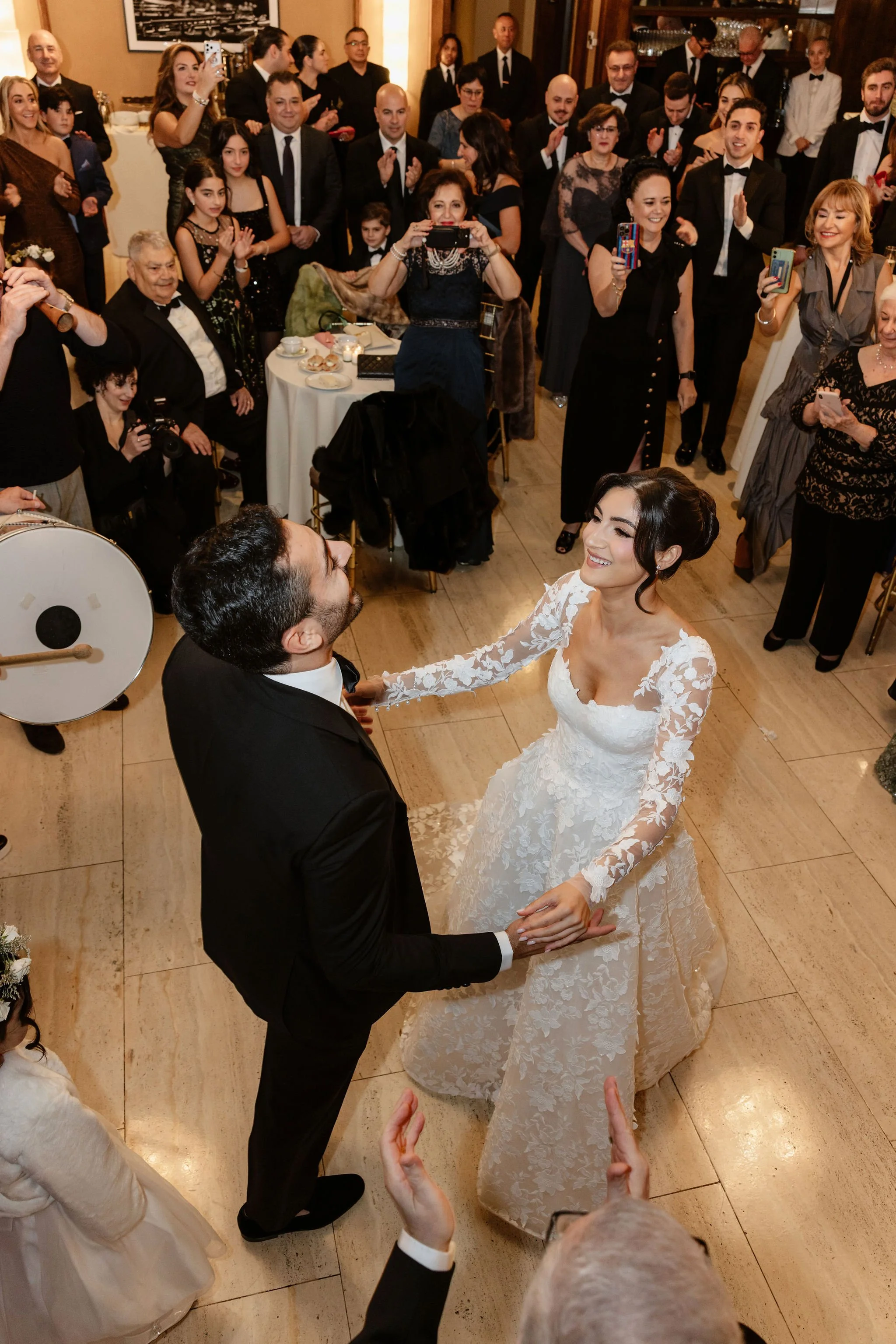 A bride and groom dancing at a wedding reception, surrounded by guests who are clapping and taking photos.