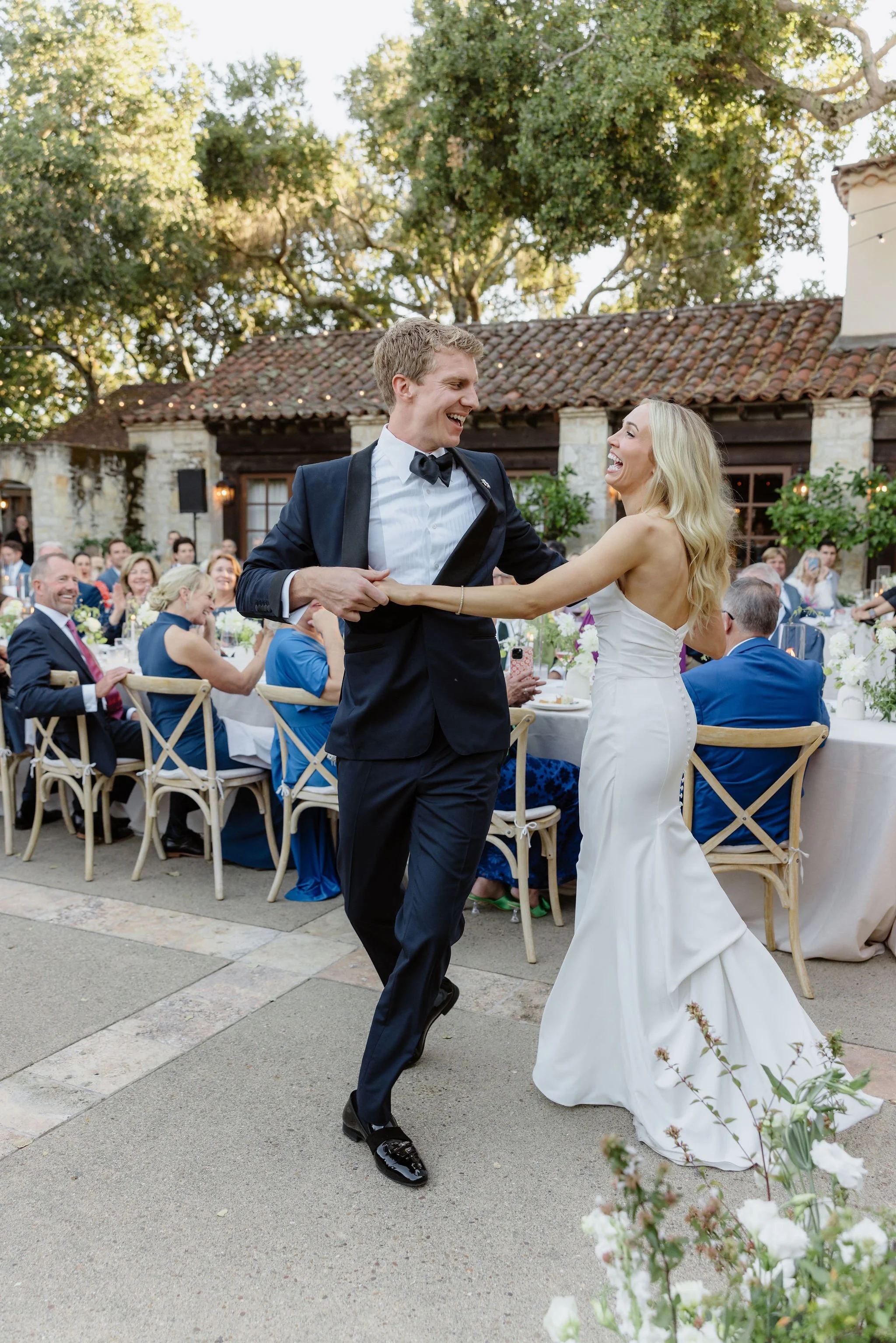 A bride and groom dancing outdoors at a wedding reception with seated guests in the background.
