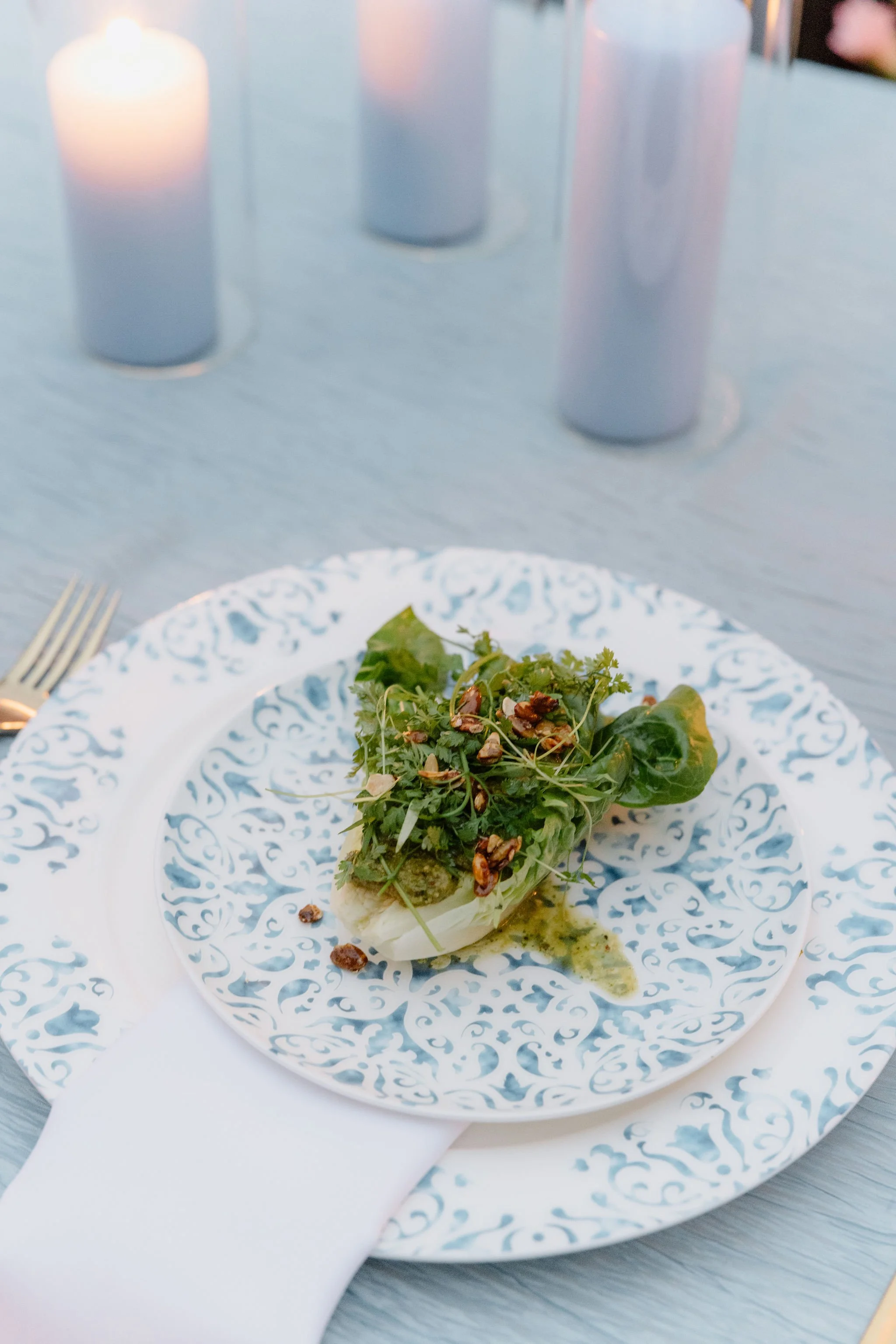 A plate of food with greens, chopped nuts, and a creamy sauce, set on a decorative blue and white patterned plate.