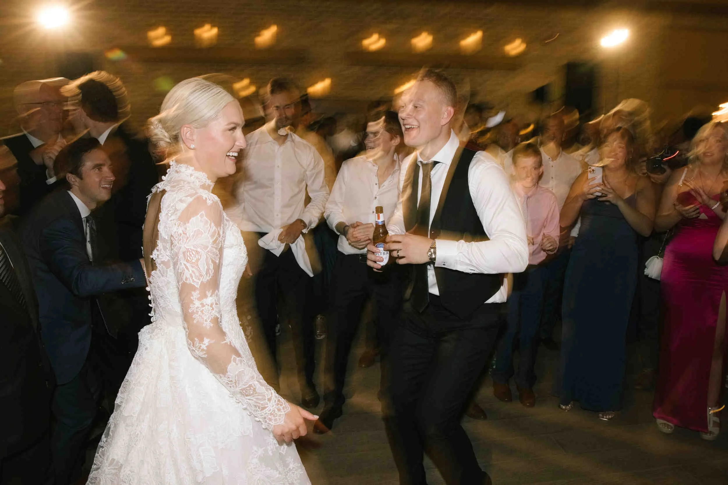 A bride and groom dancing at a wedding reception, surrounded by guests smiling and enjoying the celebration.