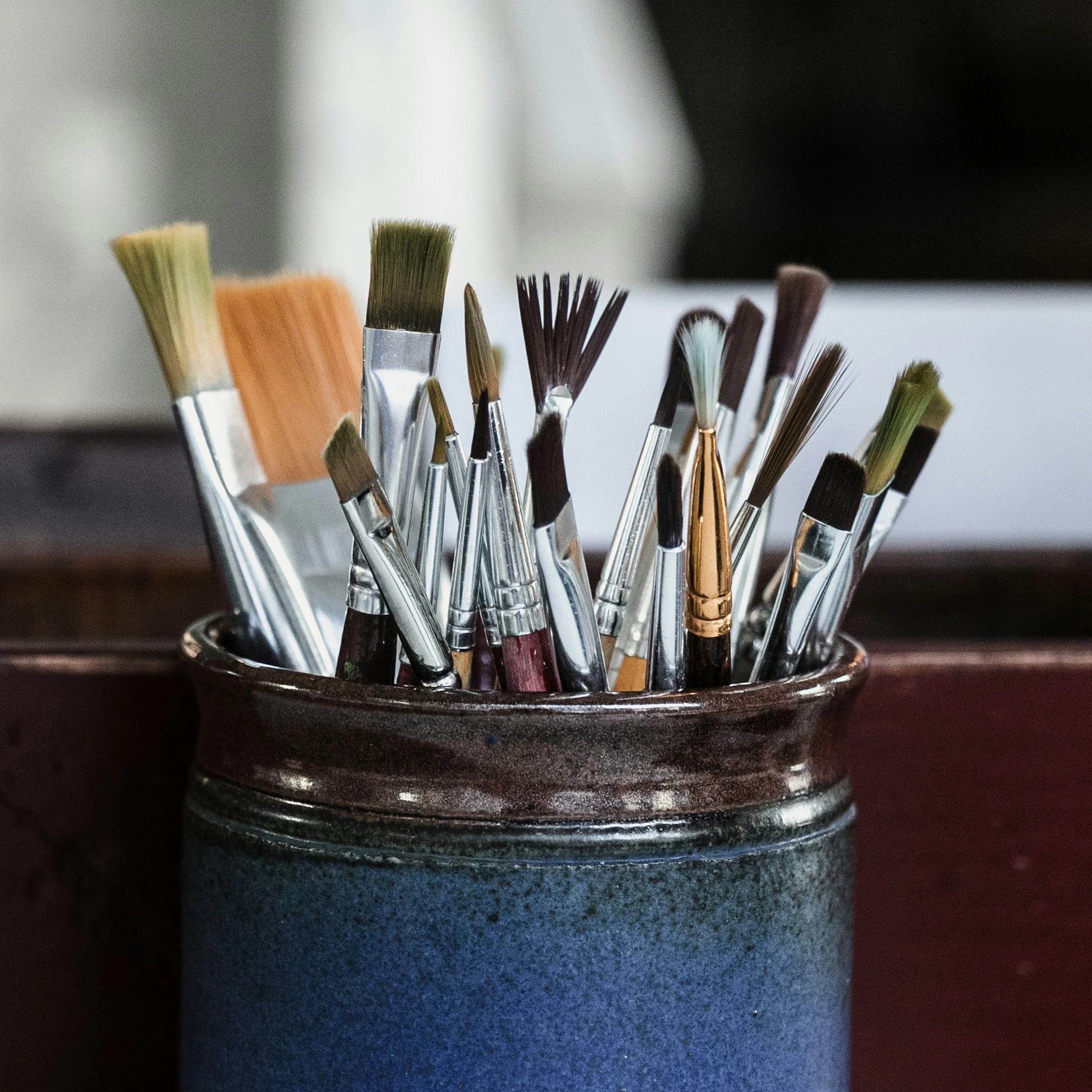 Collection of paintbrushes in a ceramic container, representing plein‑air painting tools