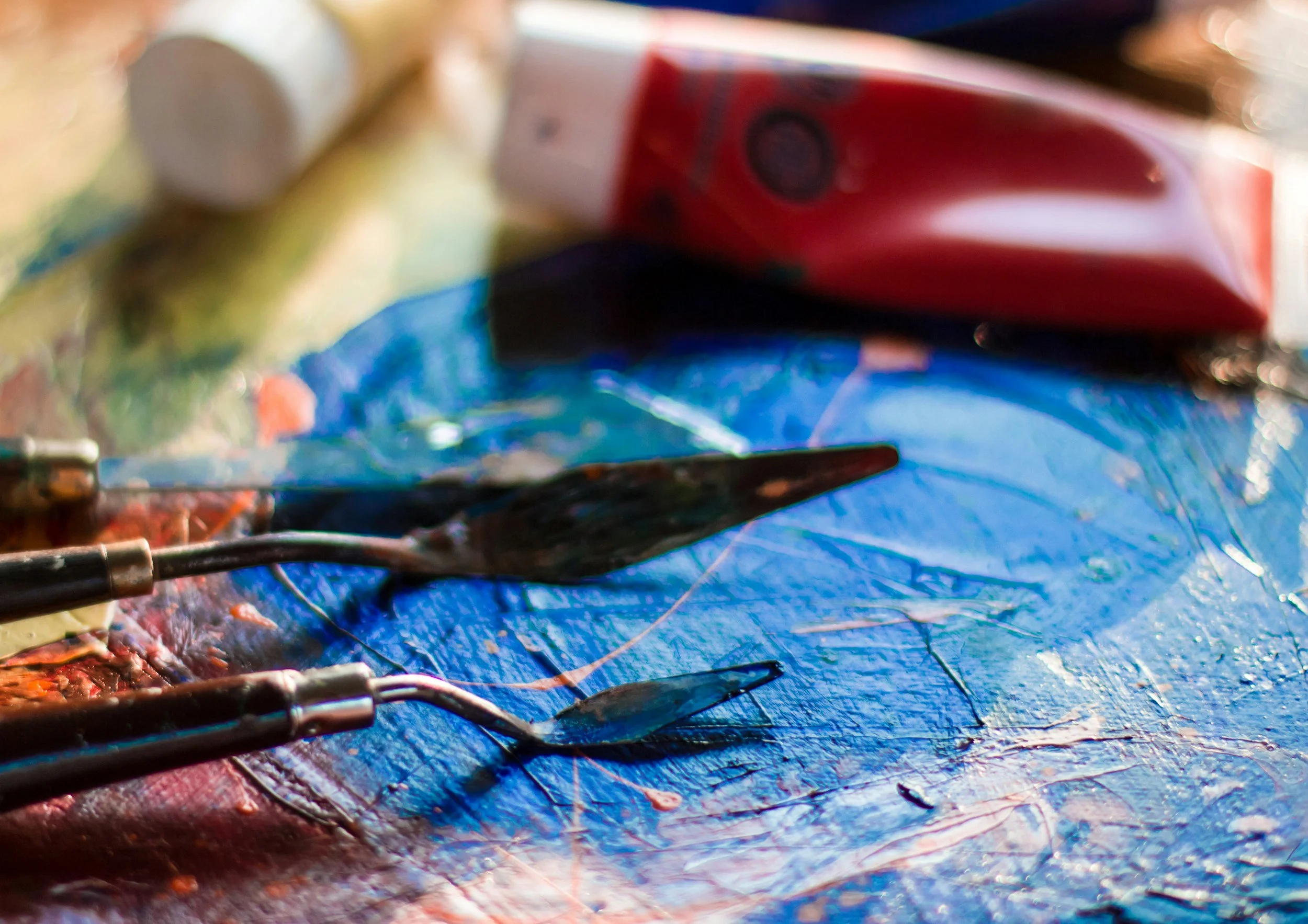 Close‑up of palette knives and brushes on a painted surface, highlighting the tools used in outdoor art sessions