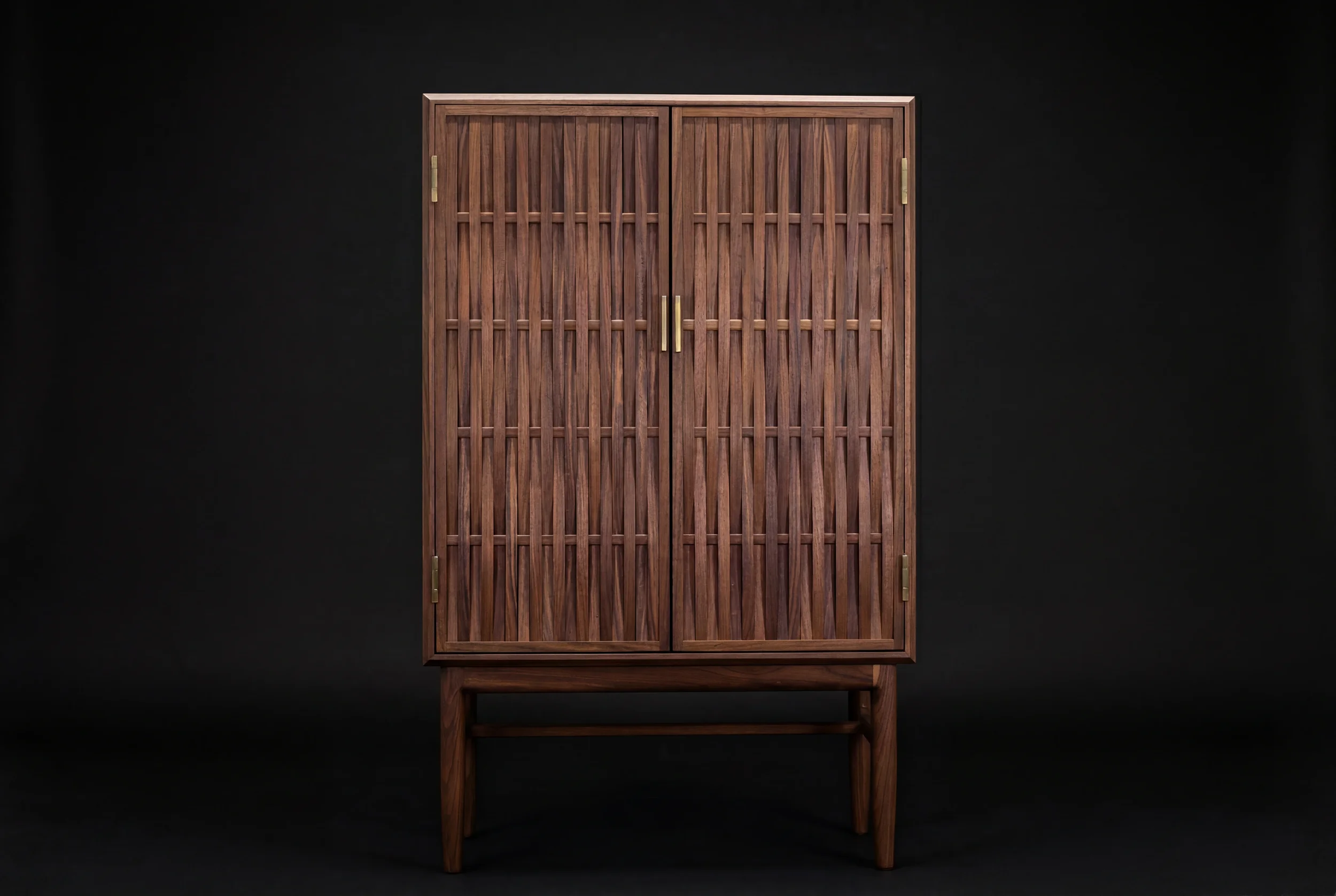 A wooden cabinet with vertical slats on the doors and brass handles, standing against a black background.