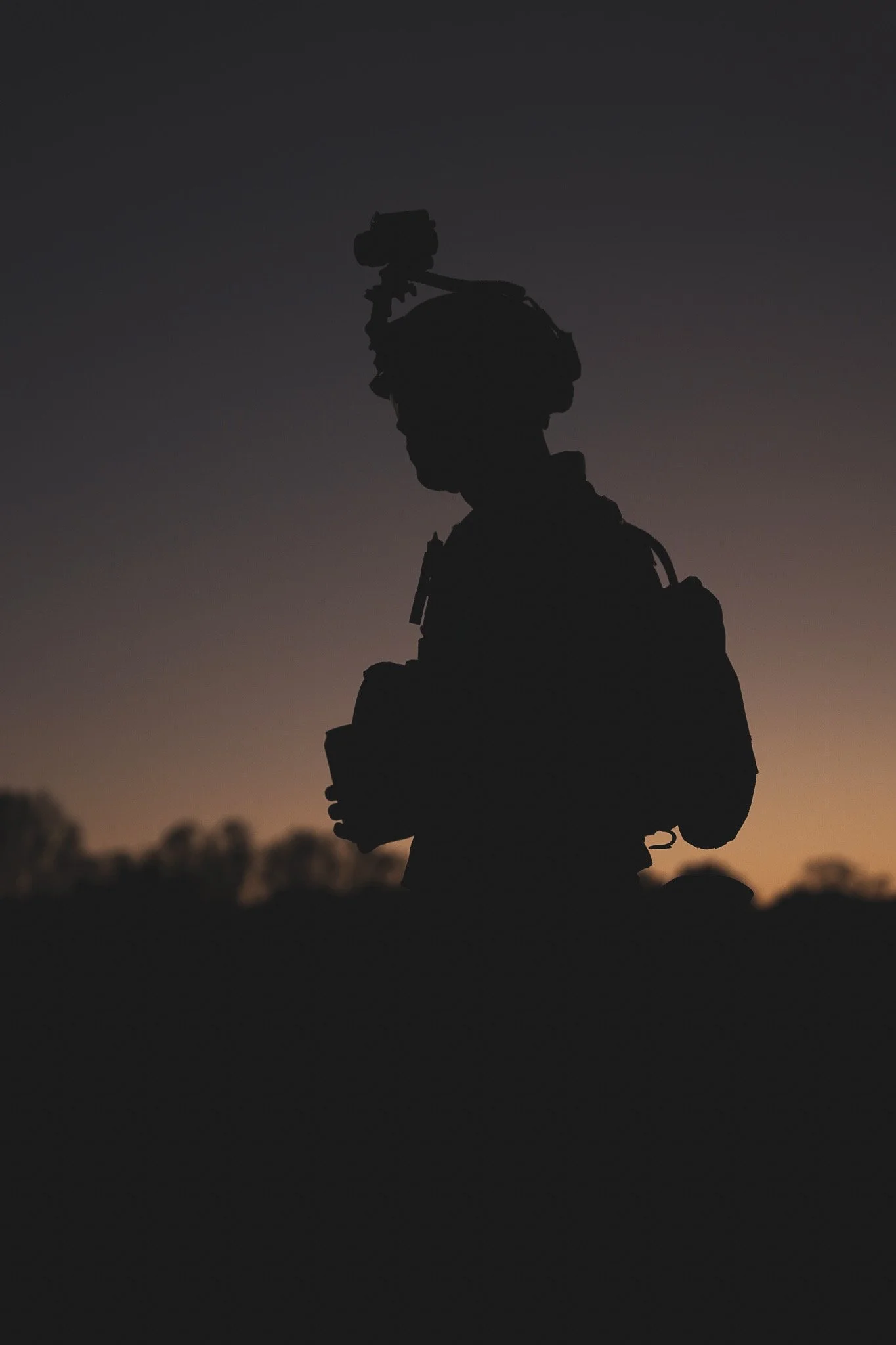 Silhouette of a soldier standing on rocks during sunset or dusk, with a clear sky in the background.